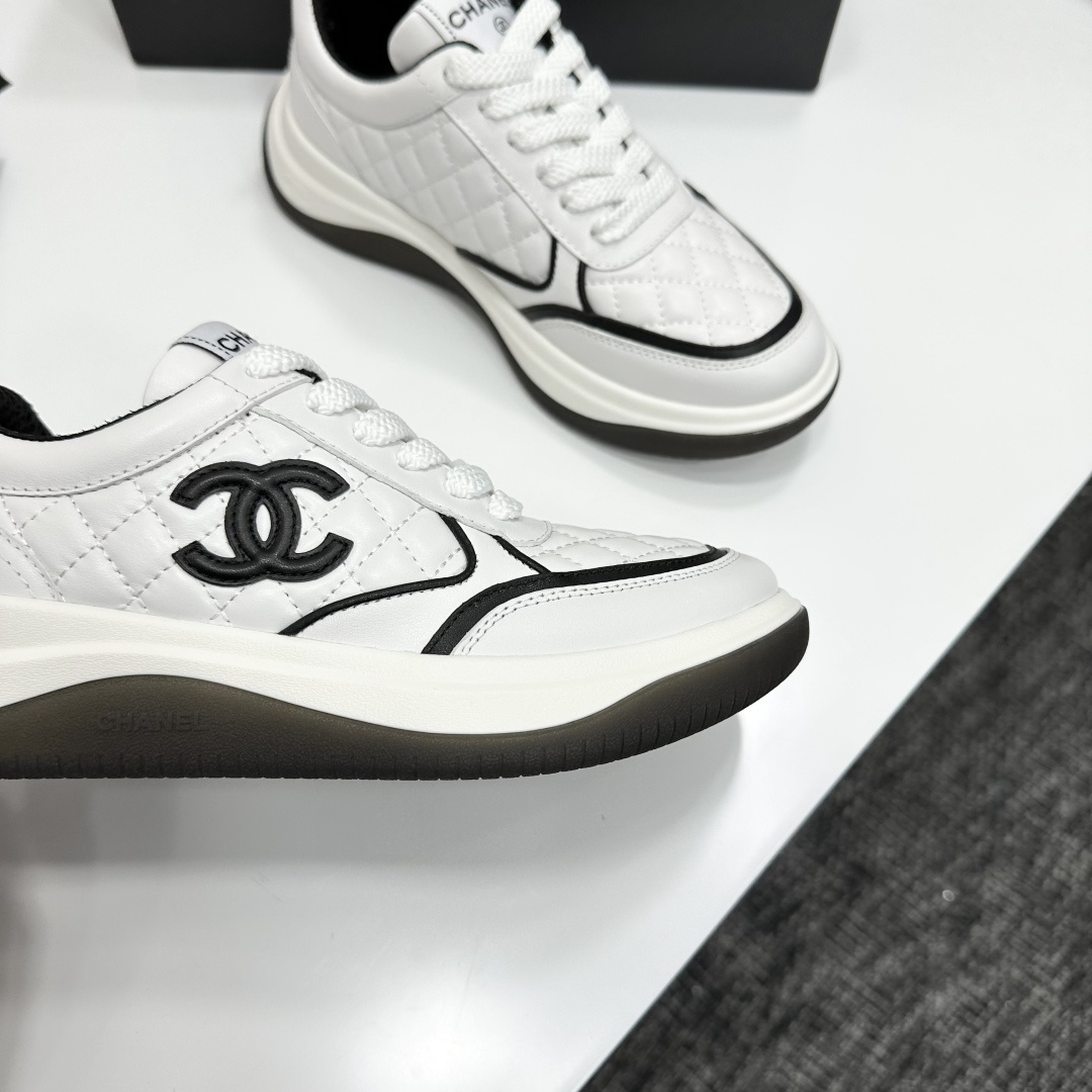 A pair of luxury Chanel white quilted leather sneakers with black CC logo and chunky soles displayed on a black box. - Hình 10