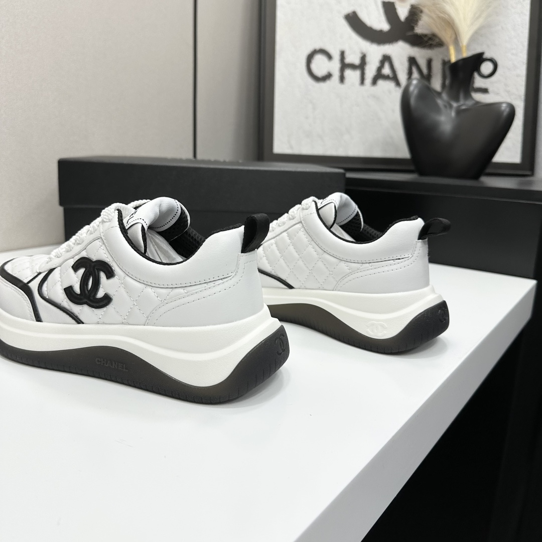 A pair of luxury Chanel white quilted leather sneakers with black CC logo and chunky soles displayed on a black box. - Hình 8