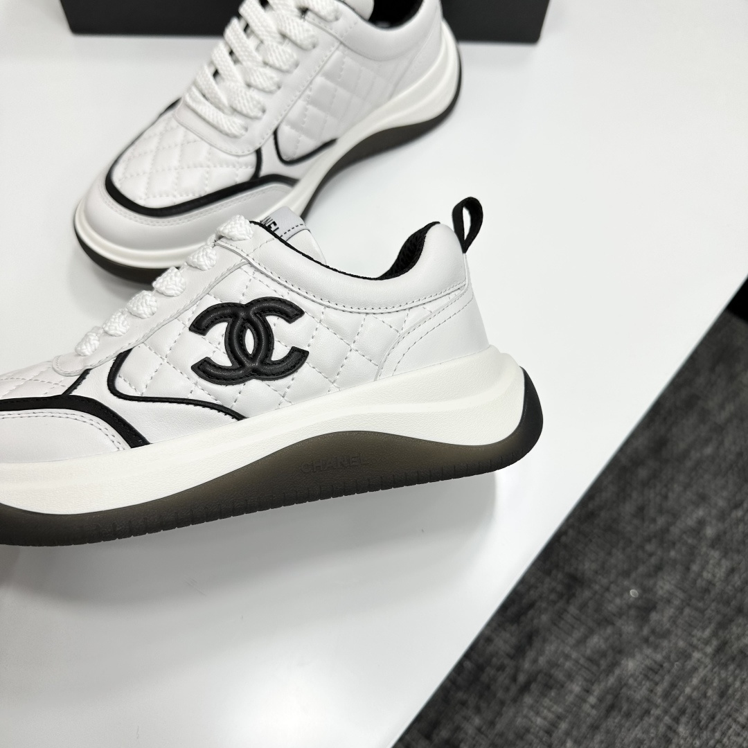 A pair of luxury Chanel white quilted leather sneakers with black CC logo and chunky soles displayed on a black box. - Hình 7
