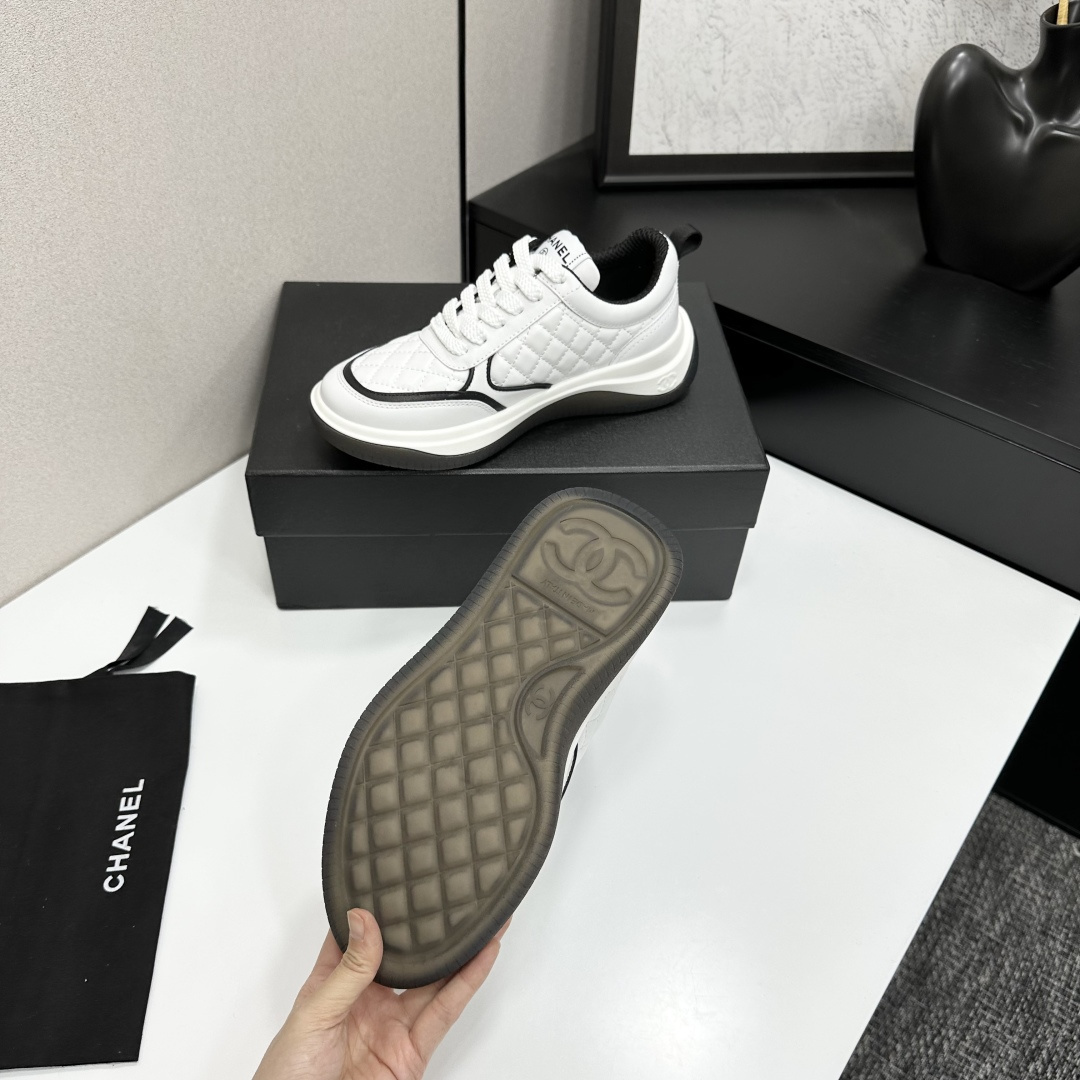 A pair of luxury Chanel white quilted leather sneakers with black CC logo and chunky soles displayed on a black box. - Hình 5