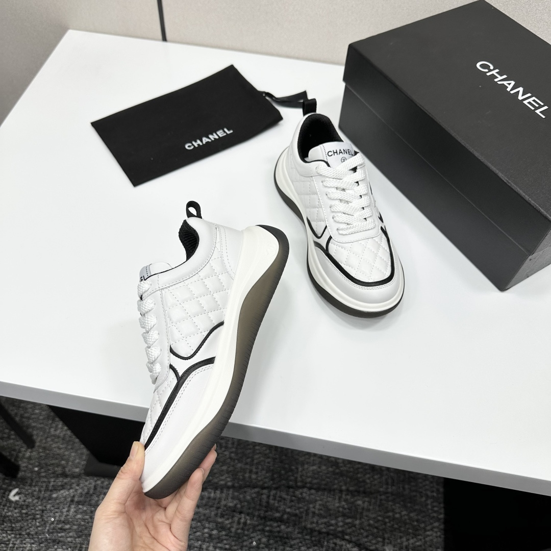 A pair of luxury Chanel white quilted leather sneakers with black CC logo and chunky soles displayed on a black box. - Hình 2