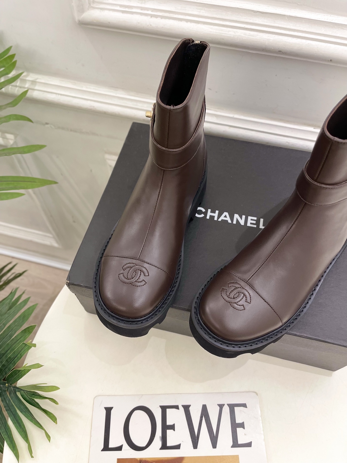 Pair of Chanel dark brown leather ankle boots with chunky black lug soles and gold CC logo hardware displayed on a black box - Hình 7