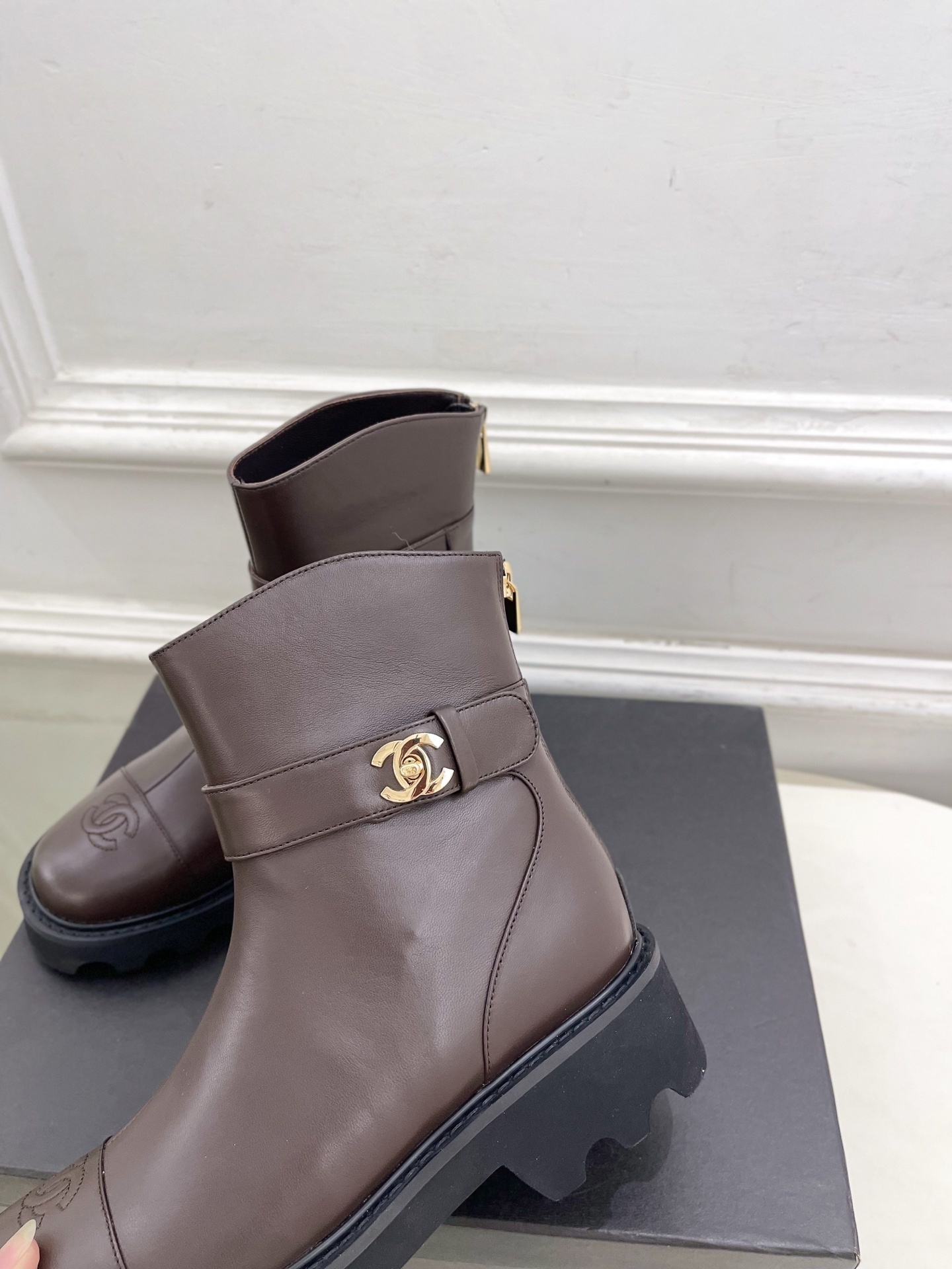 Pair of Chanel dark brown leather ankle boots with chunky black lug soles and gold CC logo hardware displayed on a black box - Hình 6