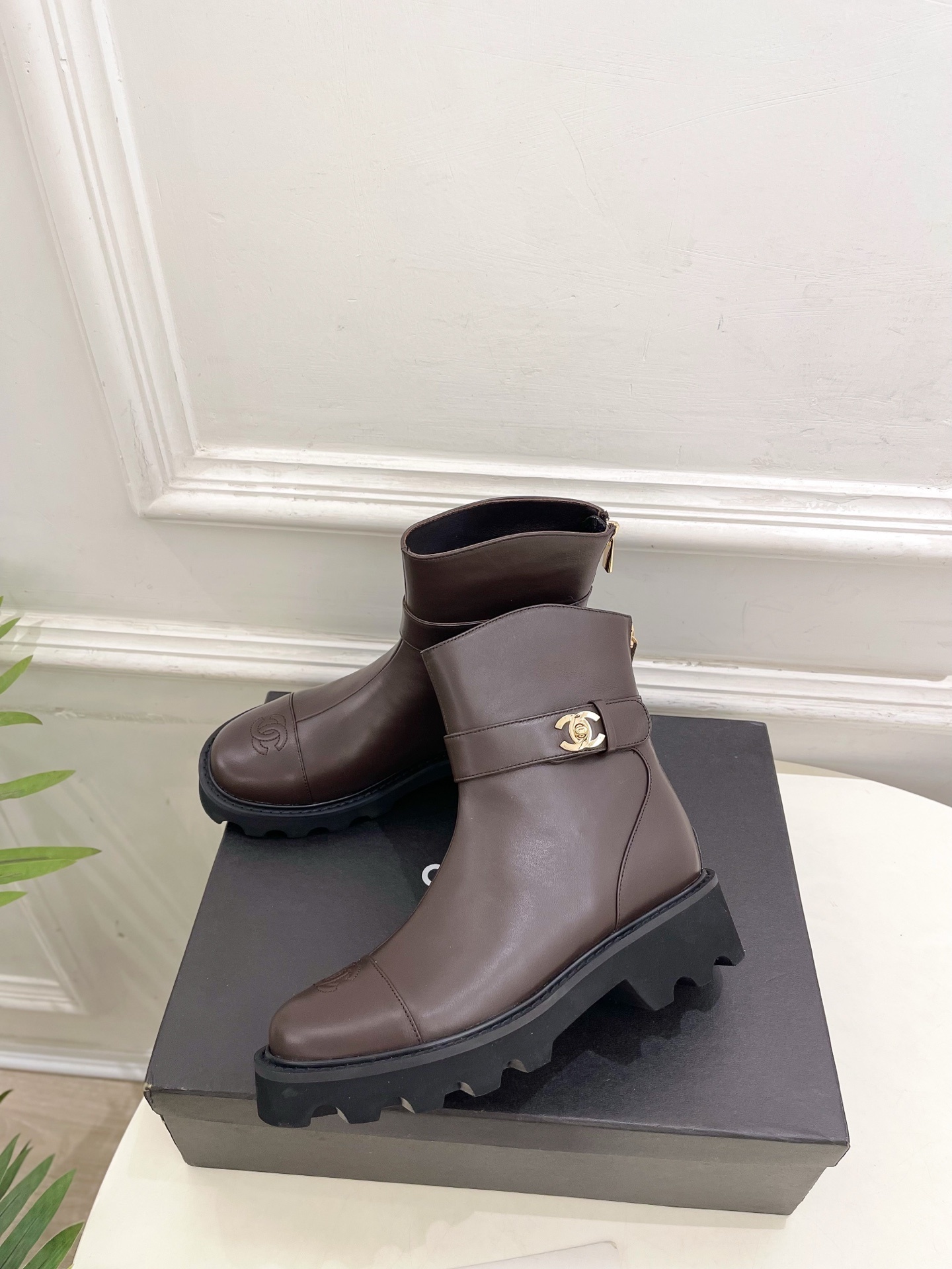 Pair of Chanel dark brown leather ankle boots with chunky black lug soles and gold CC logo hardware displayed on a black box - Hình 3