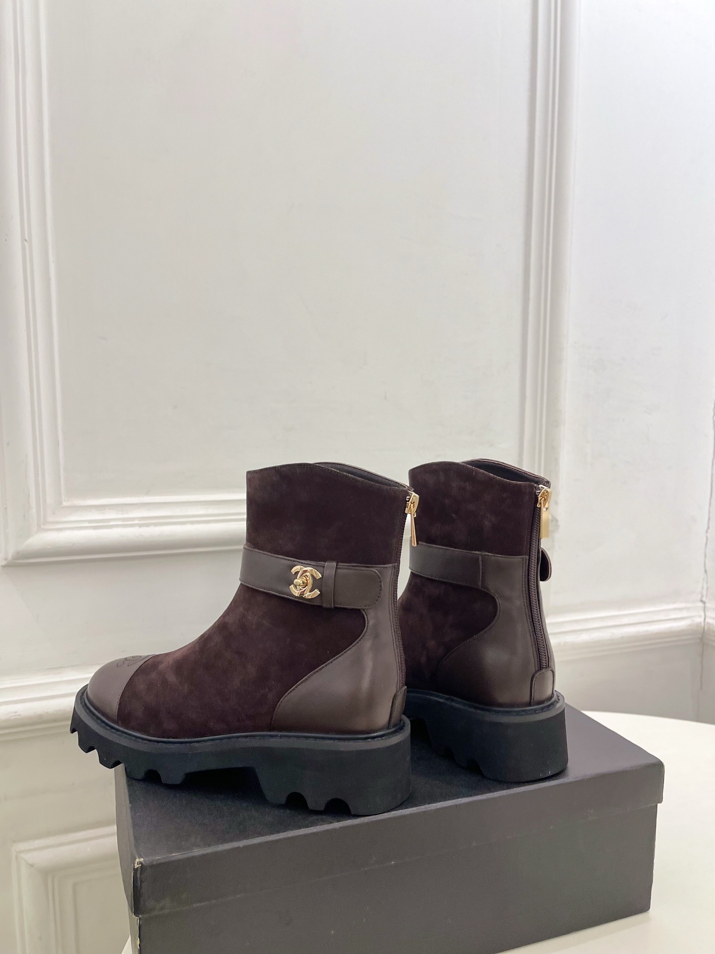 Pair of Chanel dark brown suede ankle boots with leather toe caps and gold CC logo hardware on a black box. - Hình 8