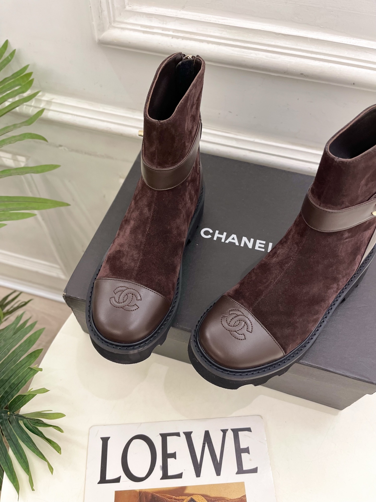 Pair of Chanel dark brown suede ankle boots with leather toe caps and gold CC logo hardware on a black box. - Hình 6