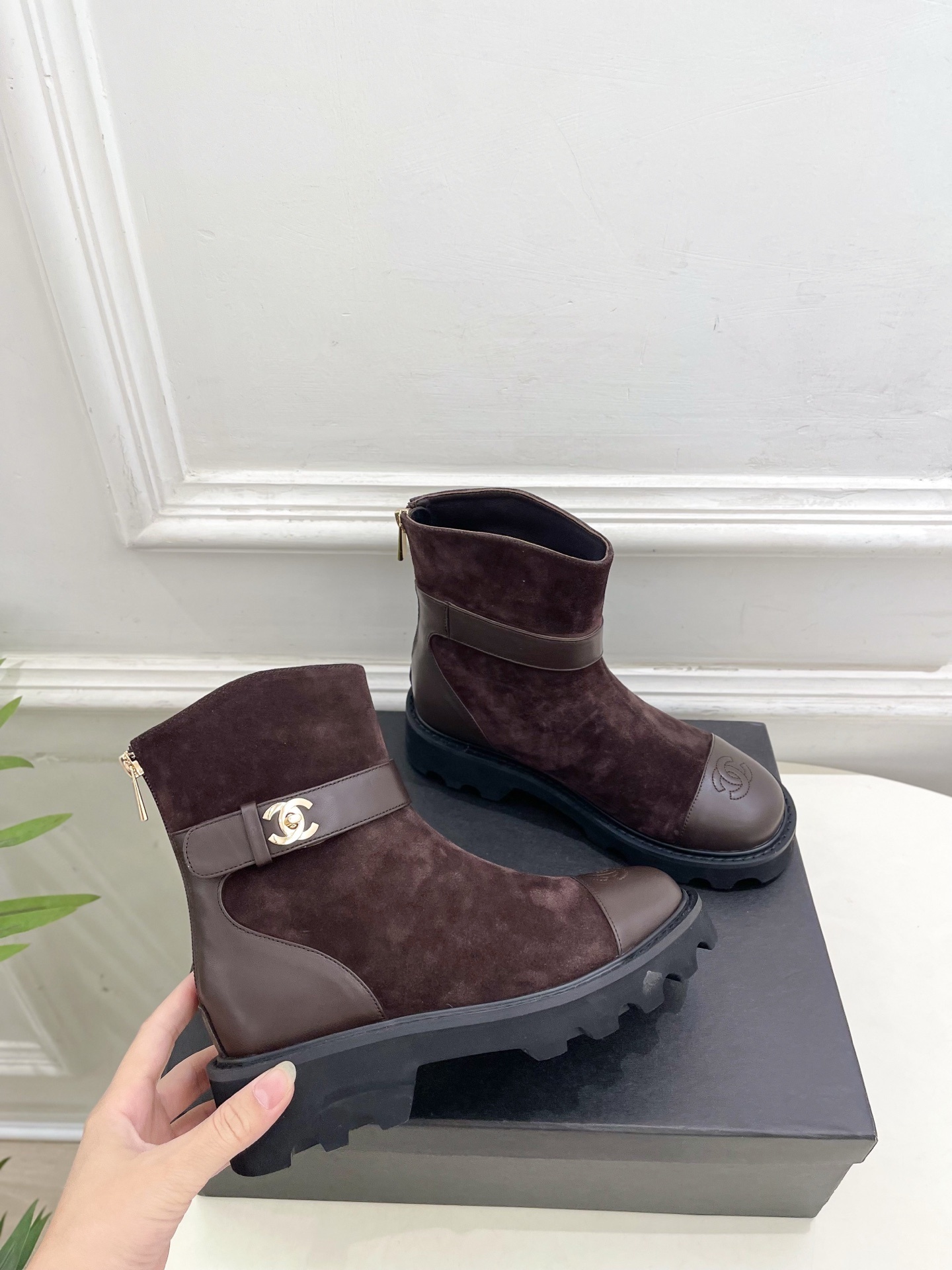 Pair of Chanel dark brown suede ankle boots with leather toe caps and gold CC logo hardware on a black box. - Hình 4