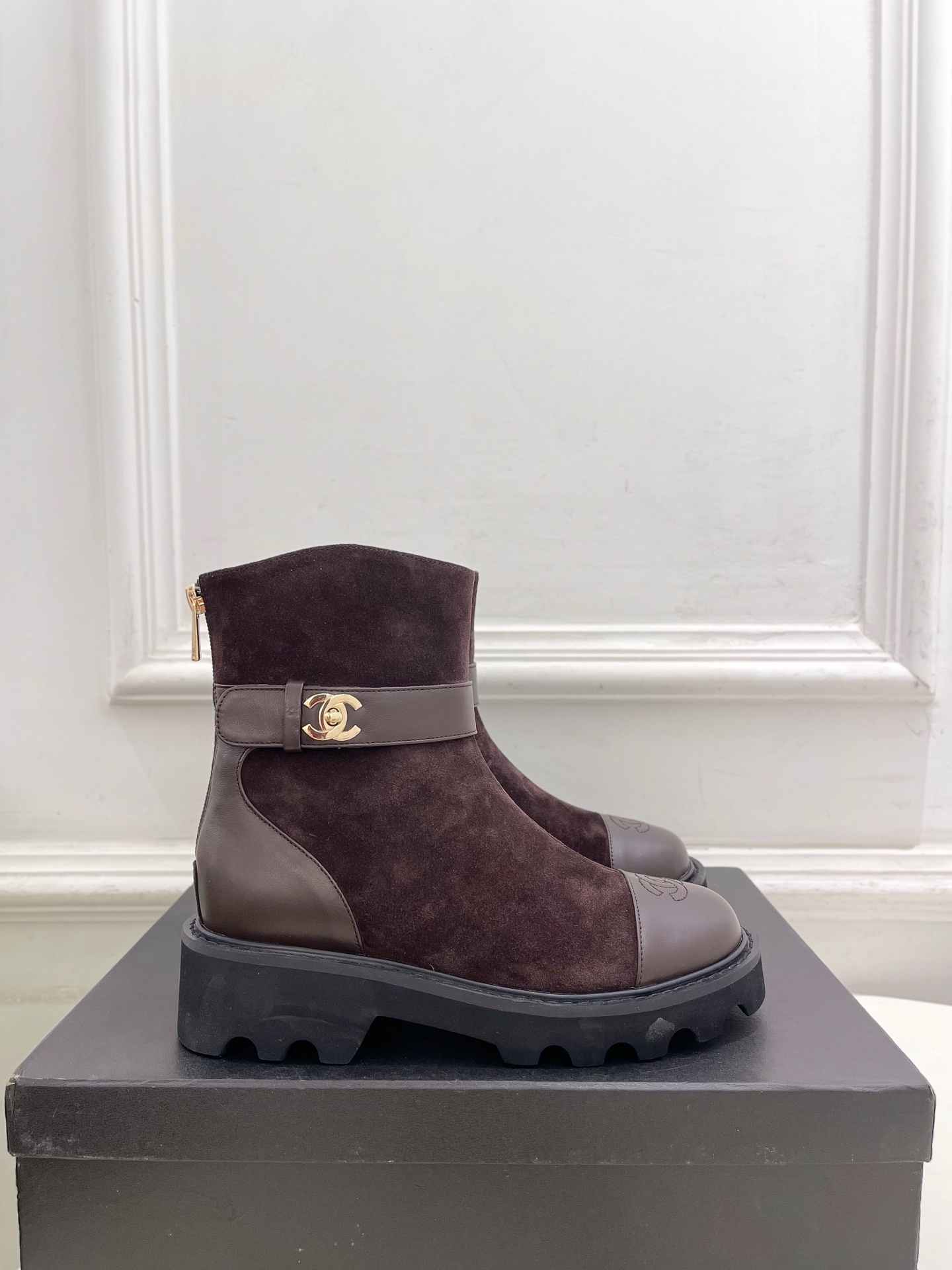 Pair of Chanel dark brown suede ankle boots with leather toe caps and gold CC logo hardware on a black box. - Hình 2