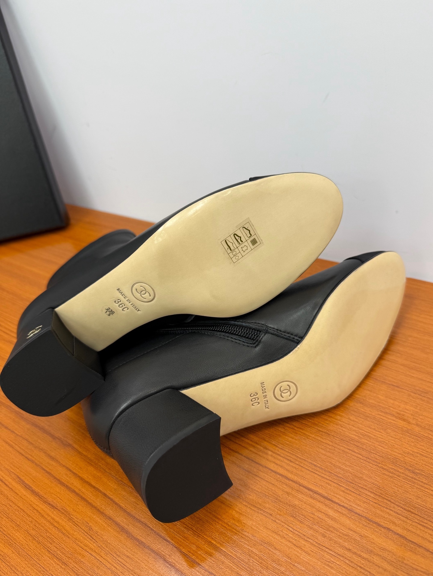 Pair of black leather ankle boots with a fabric cap toe and gold-tone side zipper on a wooden surface. - Hình 9