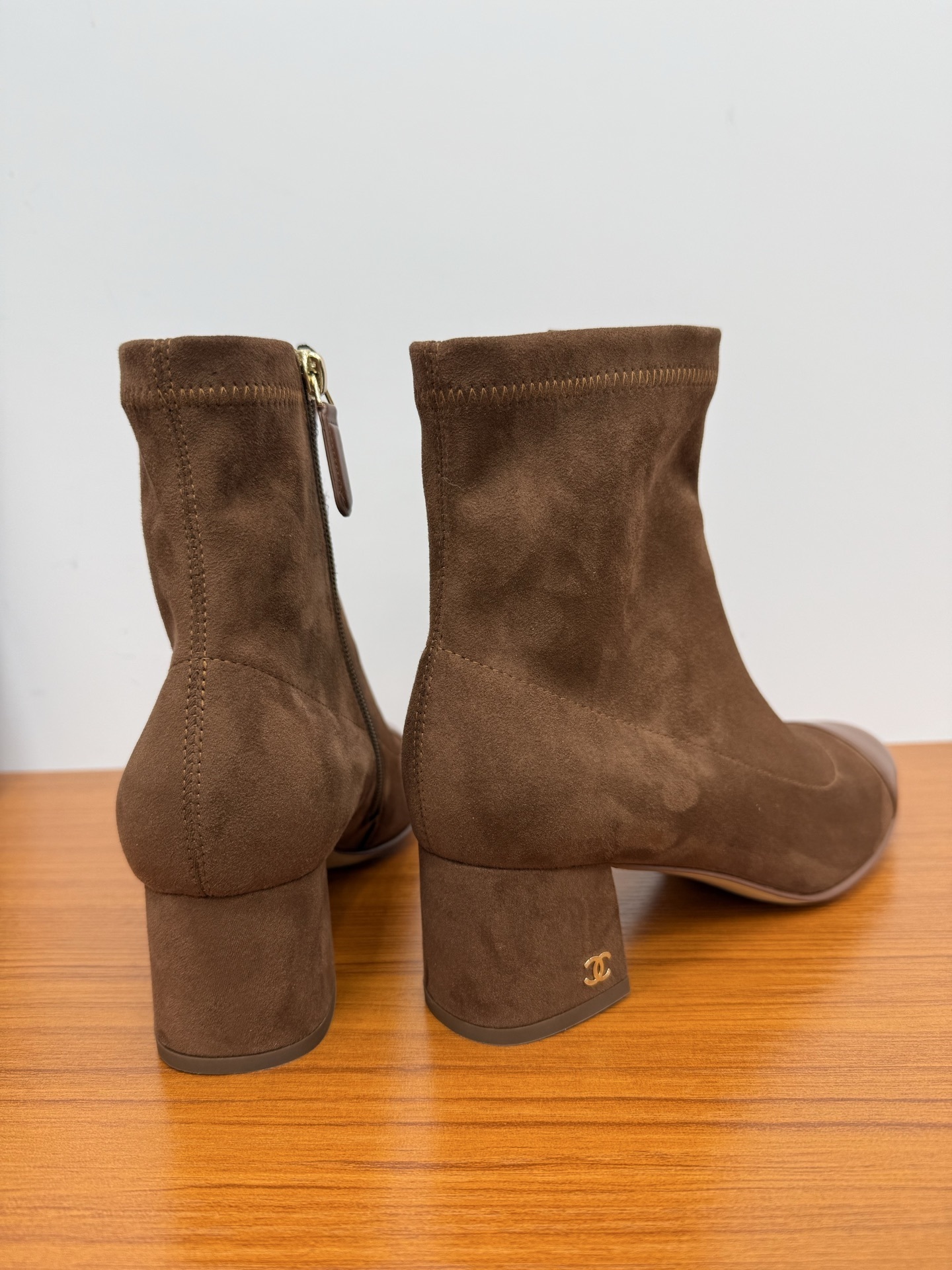 Pair of elegant brown suede ankle boots with a smooth leather toe cap and gold zipper detail on a wooden surface. - Hình 8