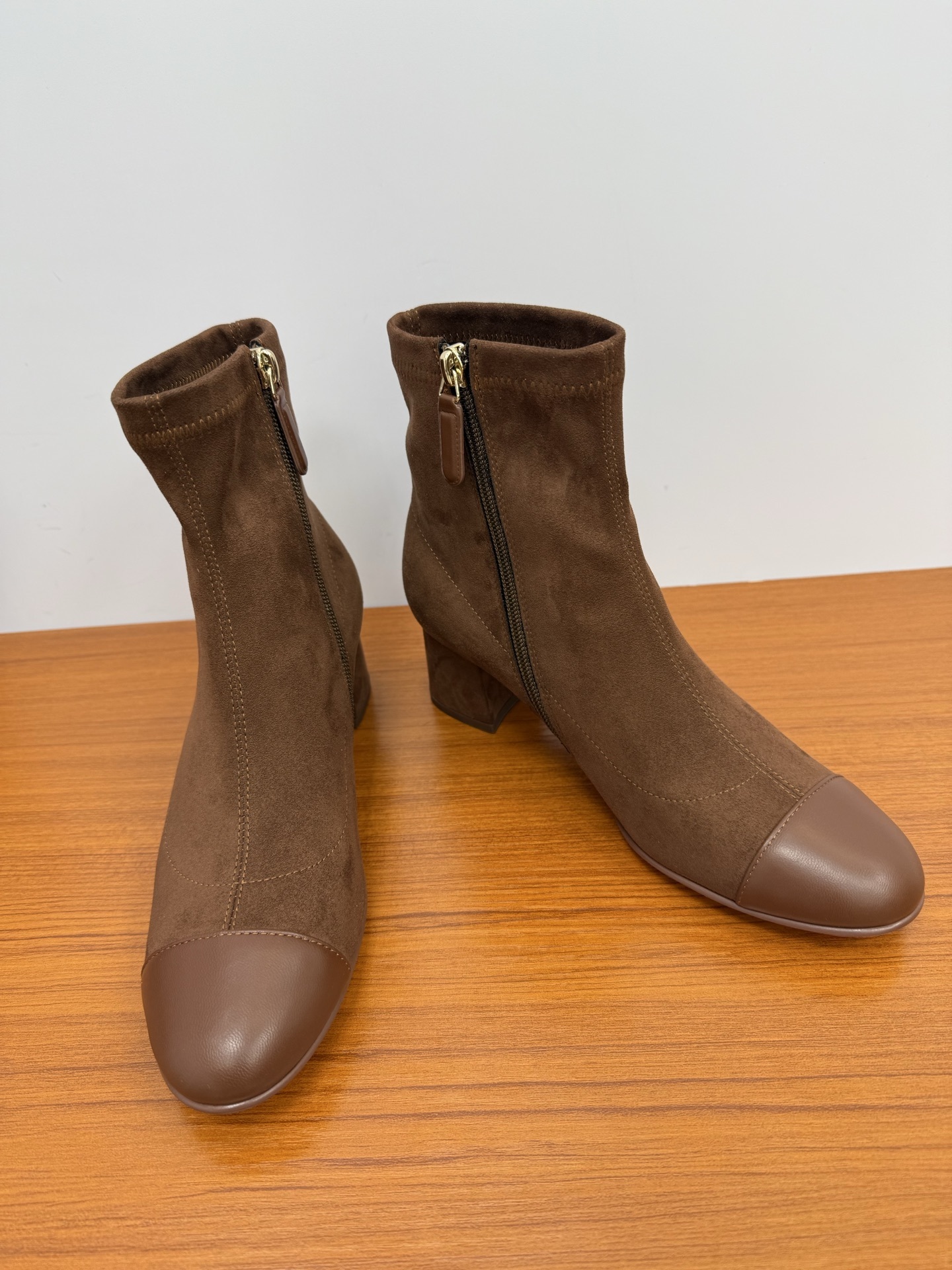 Pair of elegant brown suede ankle boots with a smooth leather toe cap and gold zipper detail on a wooden surface. - Hình 7