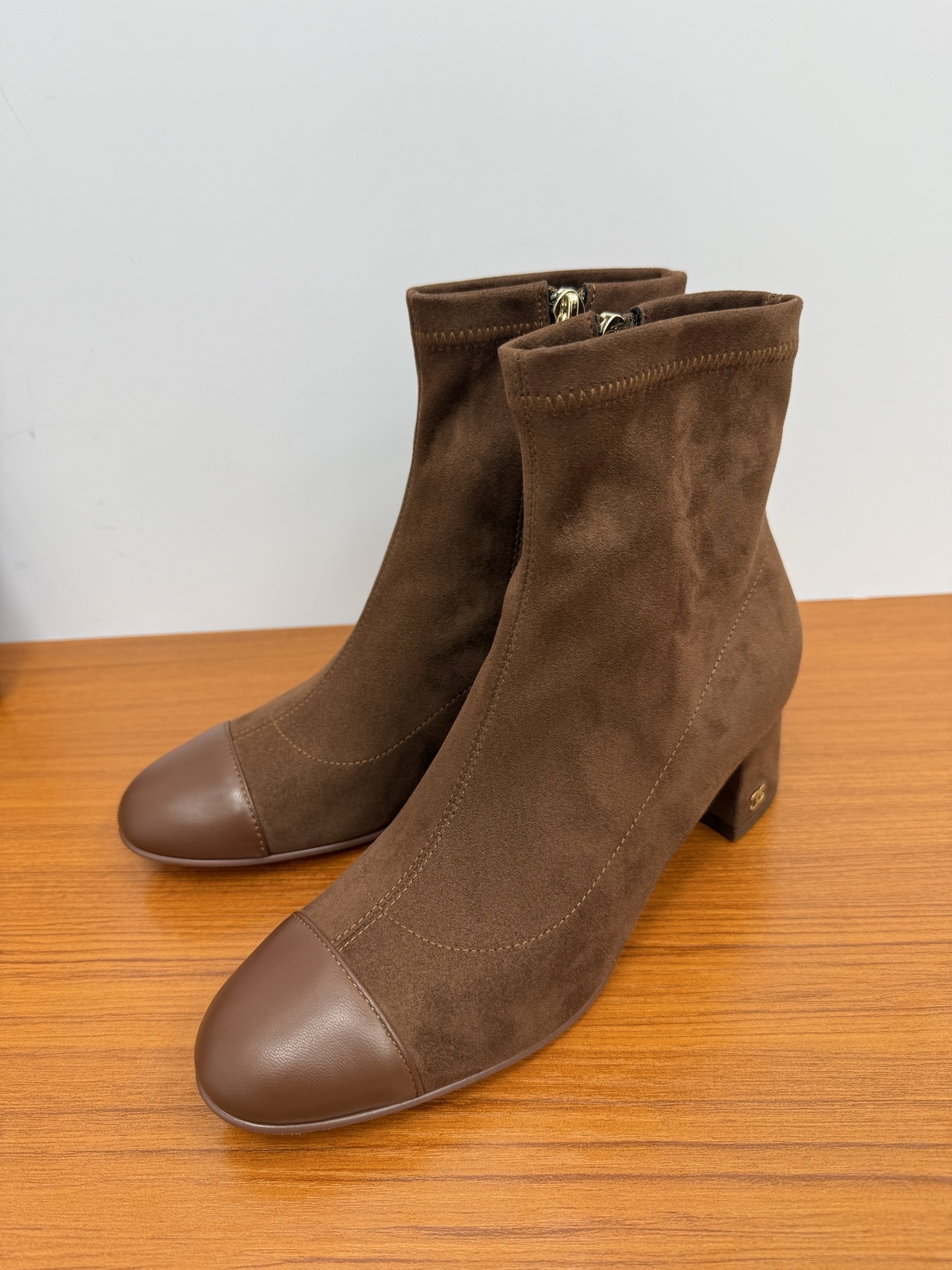 Pair of elegant brown suede ankle boots with a smooth leather toe cap and gold zipper detail on a wooden surface. - Hình 3