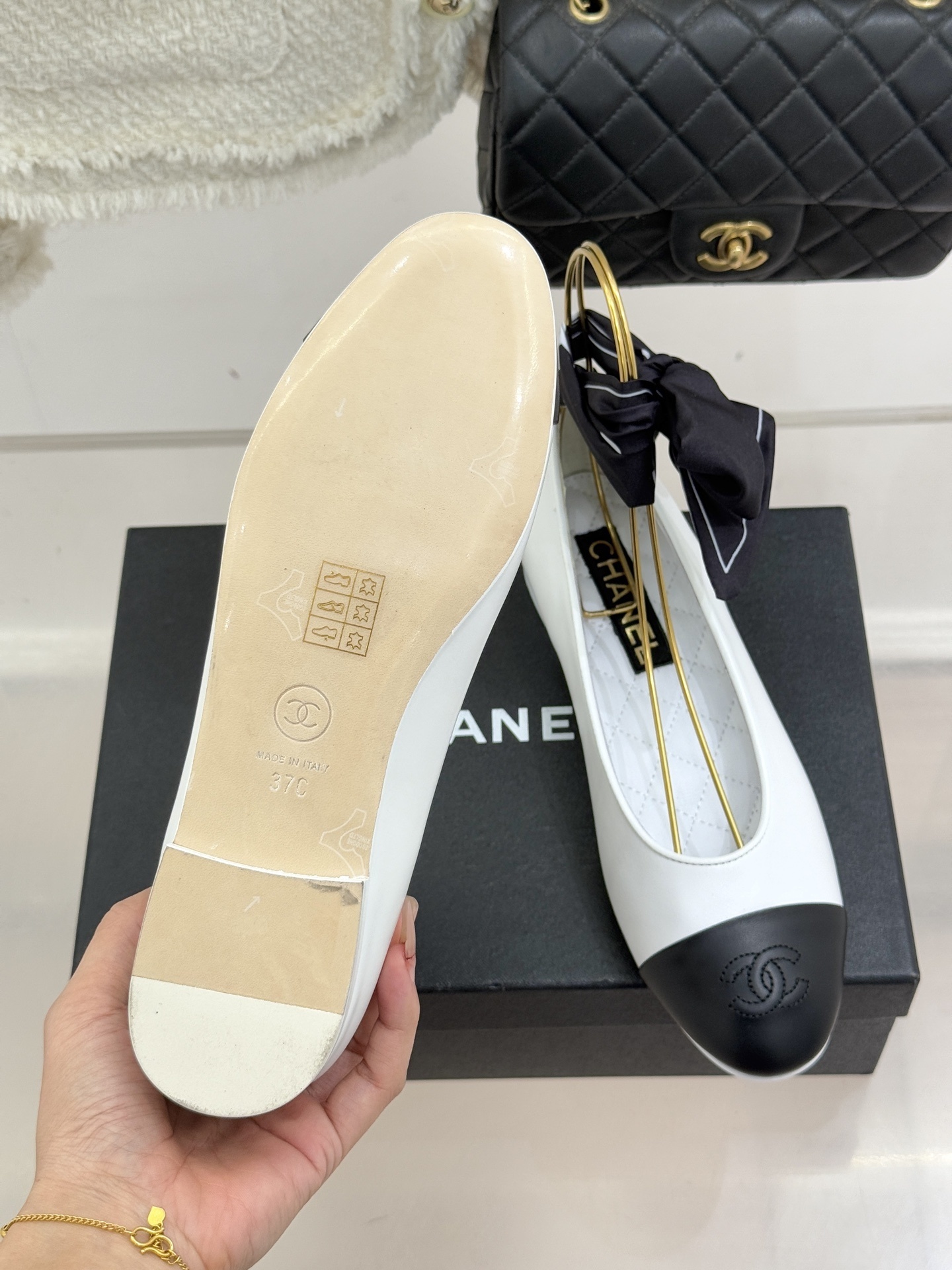 Pair of Chanel white leather ballerina flats with black cap-toe and black silk ribbon ankle ties on a black box - Hình 9