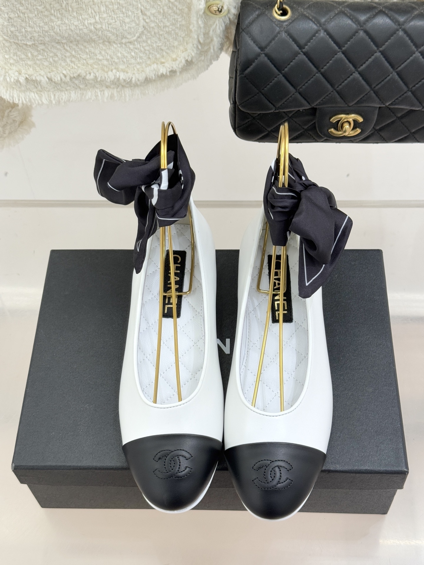 Pair of Chanel white leather ballerina flats with black cap-toe and black silk ribbon ankle ties on a black box - Hình 4