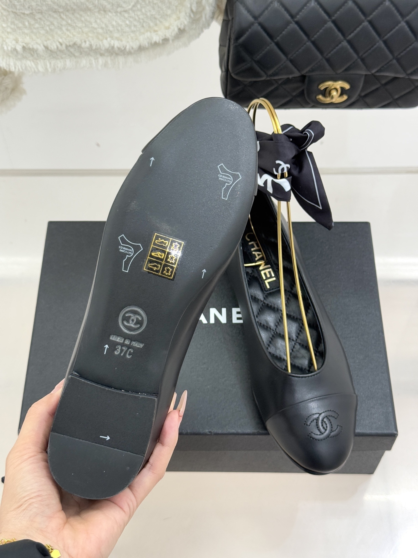 Luxury Chanel black leather ballerina flats with embossed CC logo and a black and white silk scarf ankle wrap displayed on a Chanel box. - Hình 9