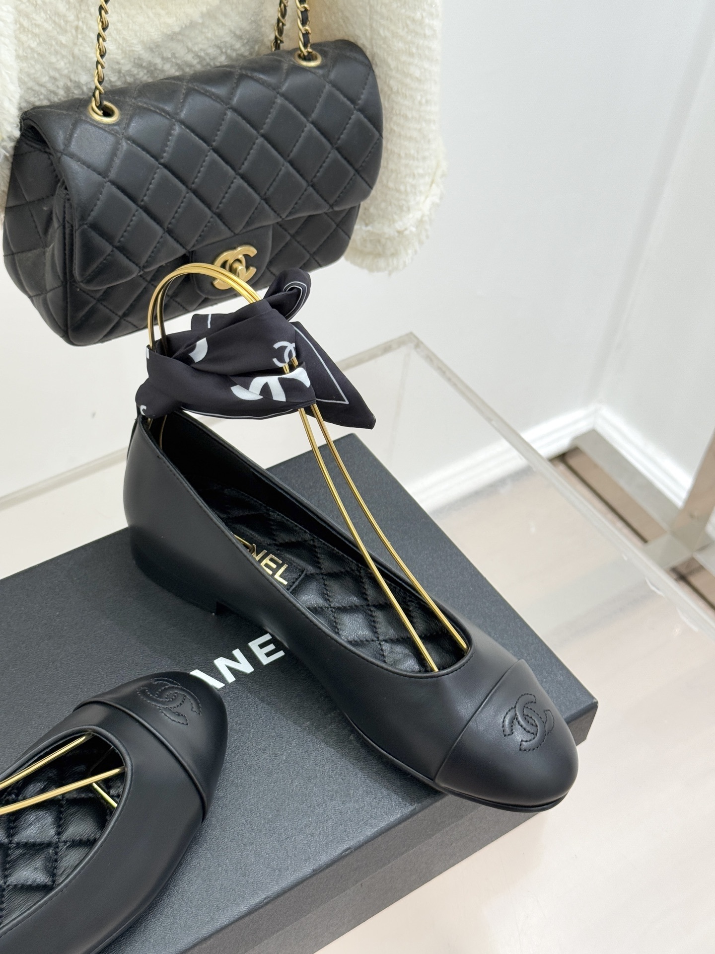 Luxury Chanel black leather ballerina flats with embossed CC logo and a black and white silk scarf ankle wrap displayed on a Chanel box. - Hình 5