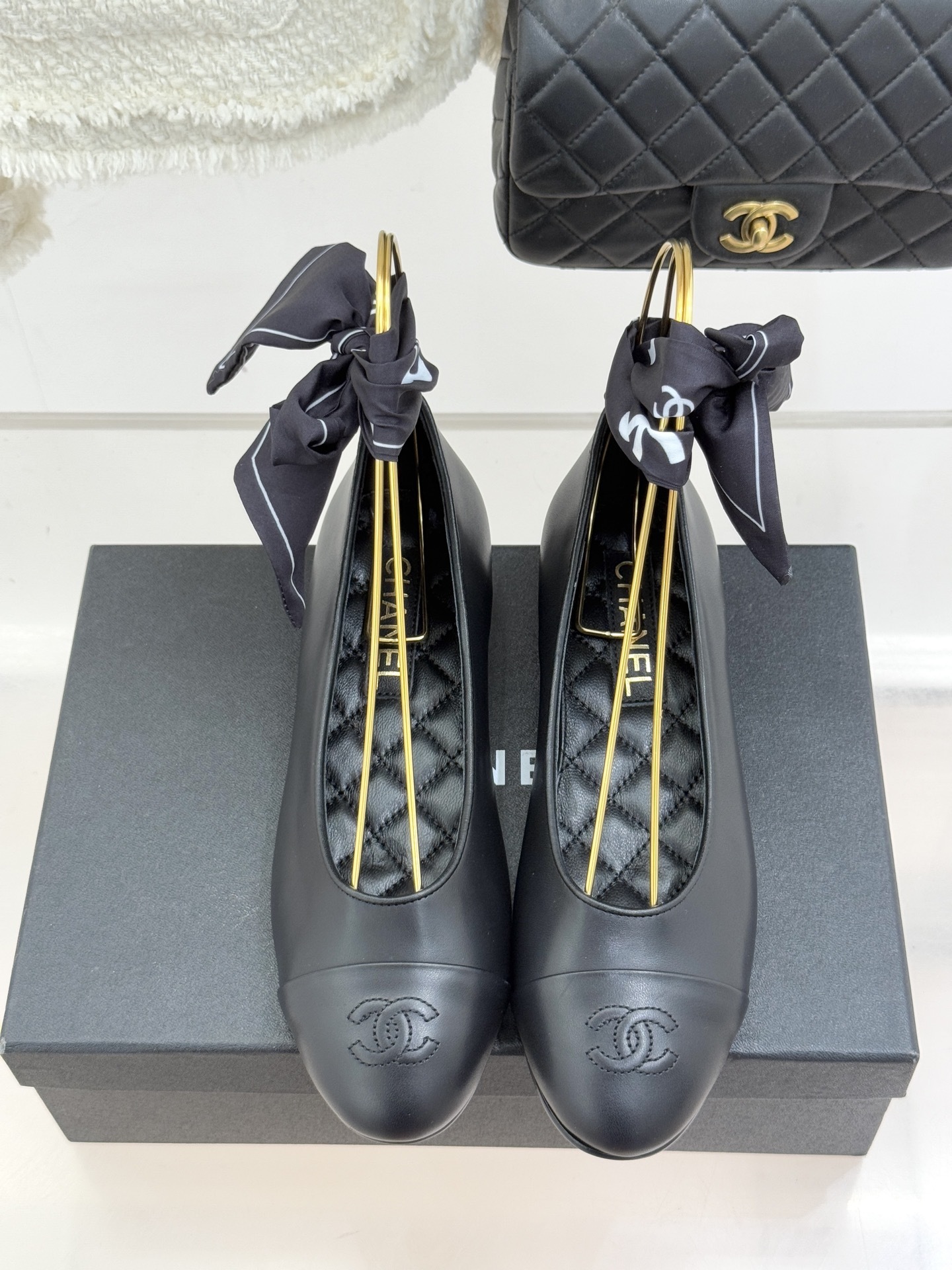 Luxury Chanel black leather ballerina flats with embossed CC logo and a black and white silk scarf ankle wrap displayed on a Chanel box. - Hình 4