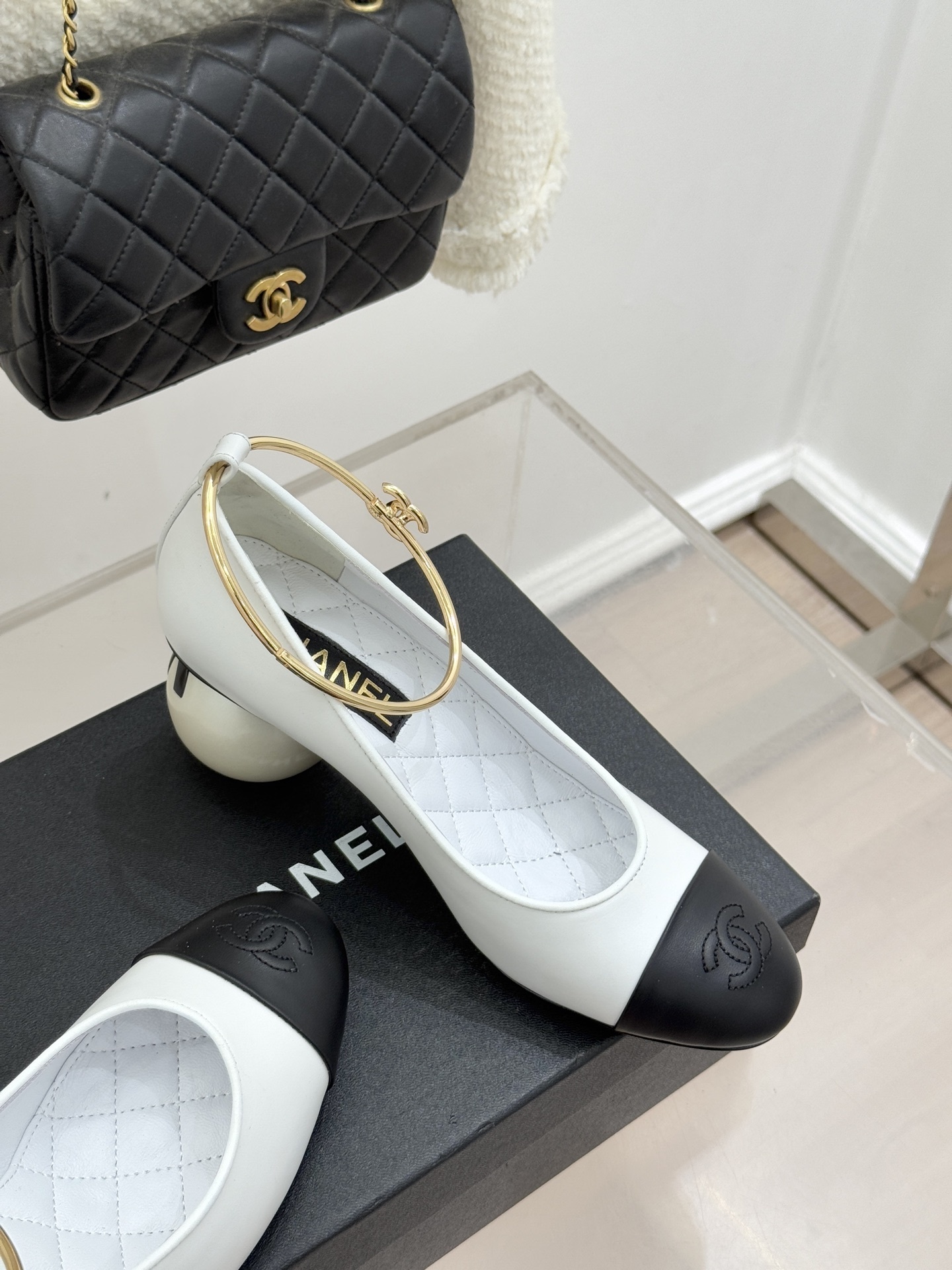 Pair of Chanel white and black bicolor pumps with a spherical pearl heel and gold-tone ankle rings displayed on a black box. - Hình 5