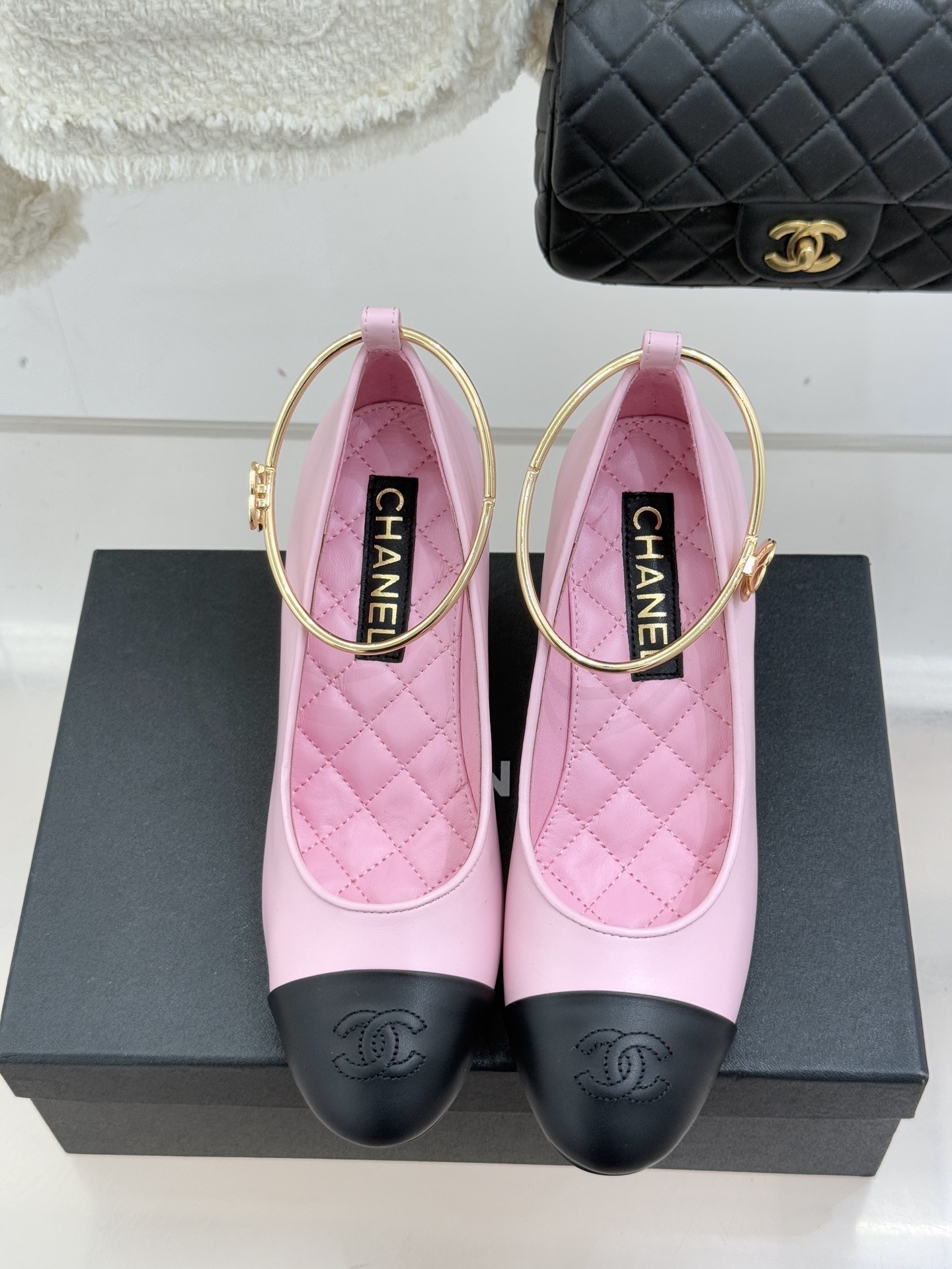 A pair of luxury pink Chanel pumps with black cap-toes, gold ankle ring details, and large pearl-shaped heels resting on a black branded box. - Hình 4