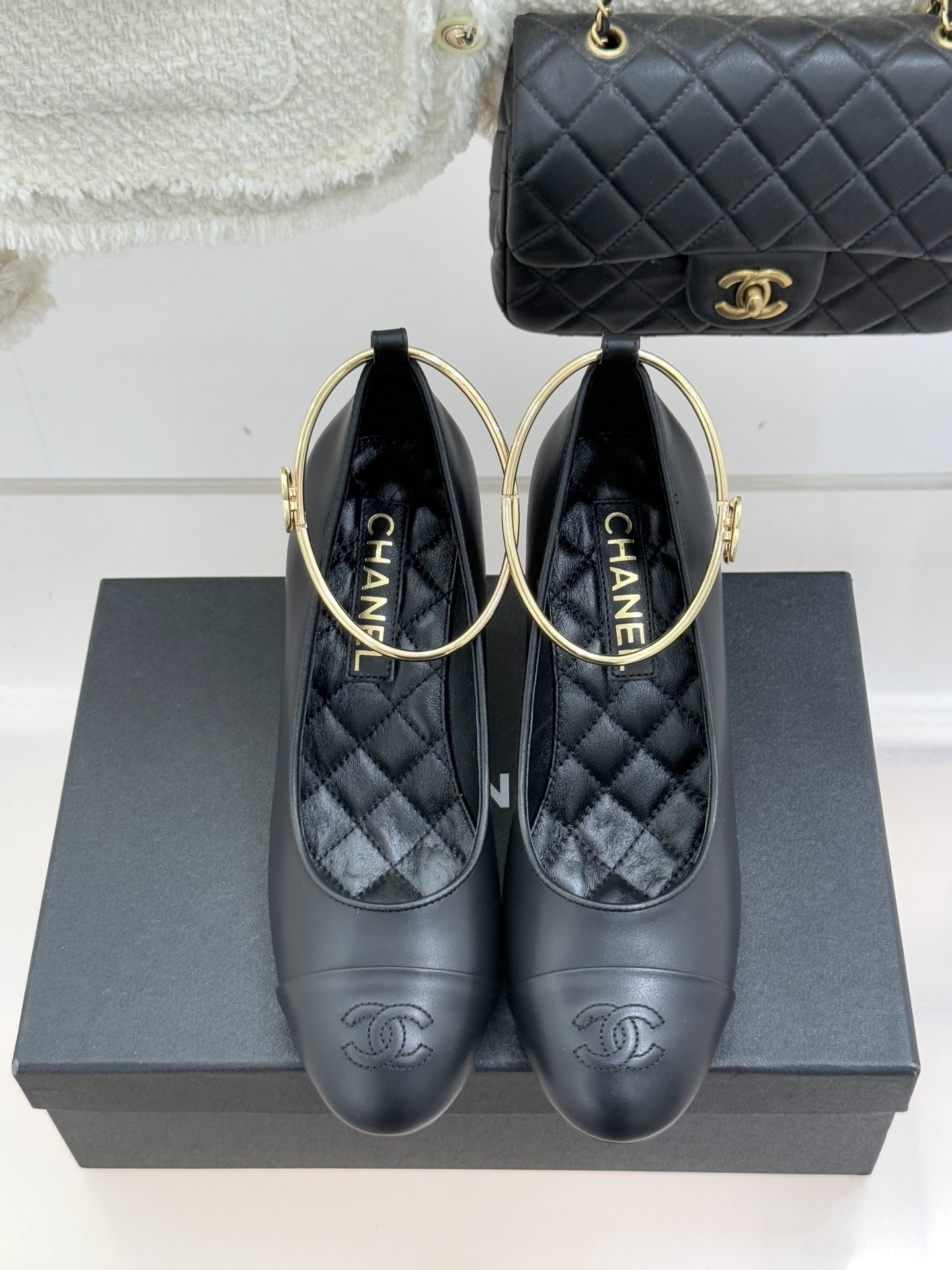 Pair of Chanel black leather pumps featuring a white round pearl heel and a gold-tone CC logo ankle ring on a black designer box. - Hình 4