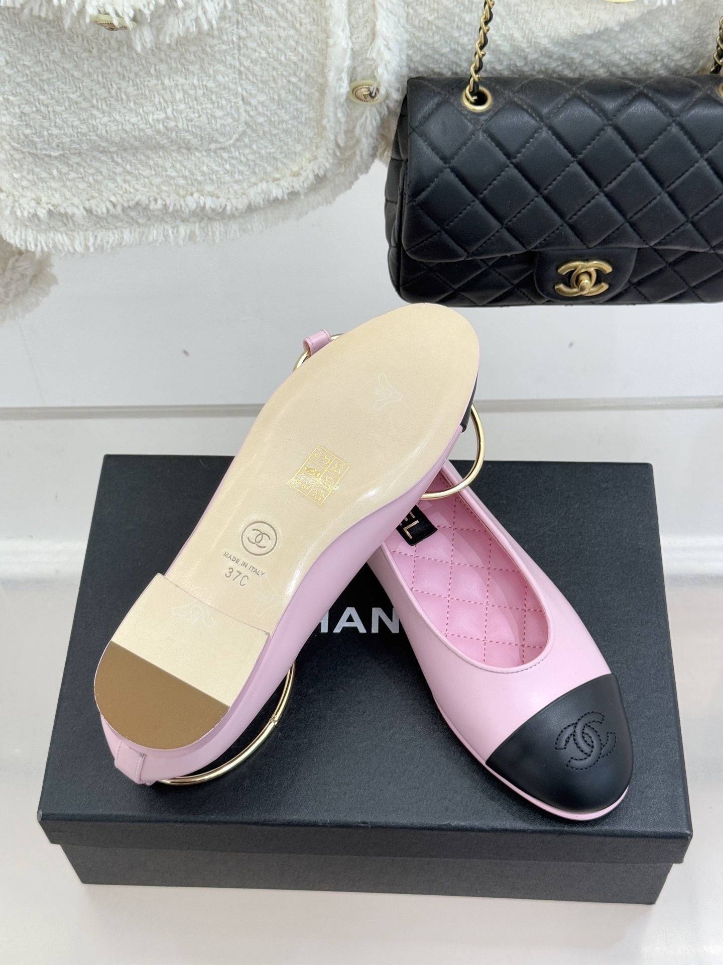 Pair of pink and black Chanel-style ballet flats with gold ankle rings resting on a black box. - Hình 9