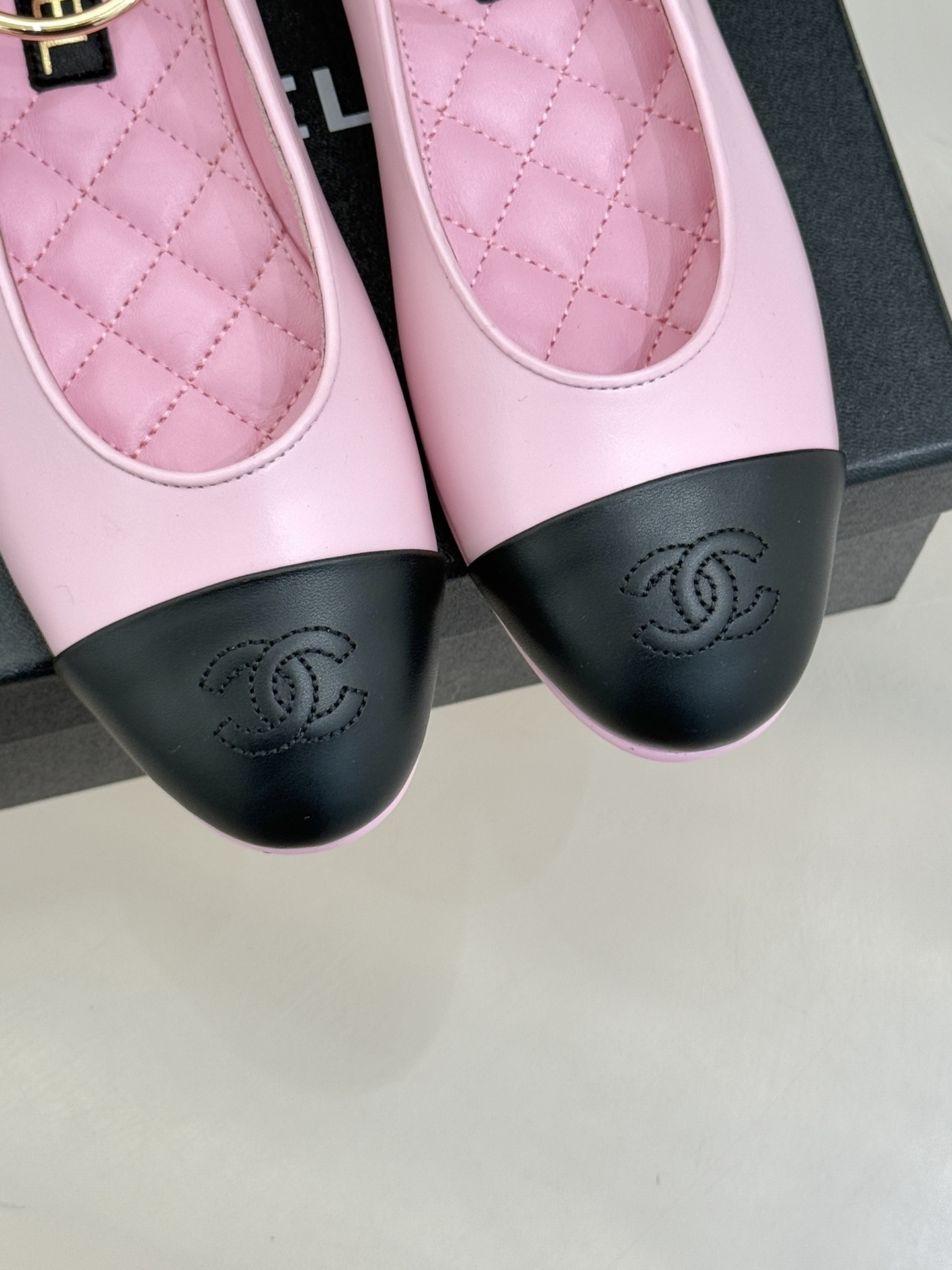 Pair of pink and black Chanel-style ballet flats with gold ankle rings resting on a black box. - Hình 7