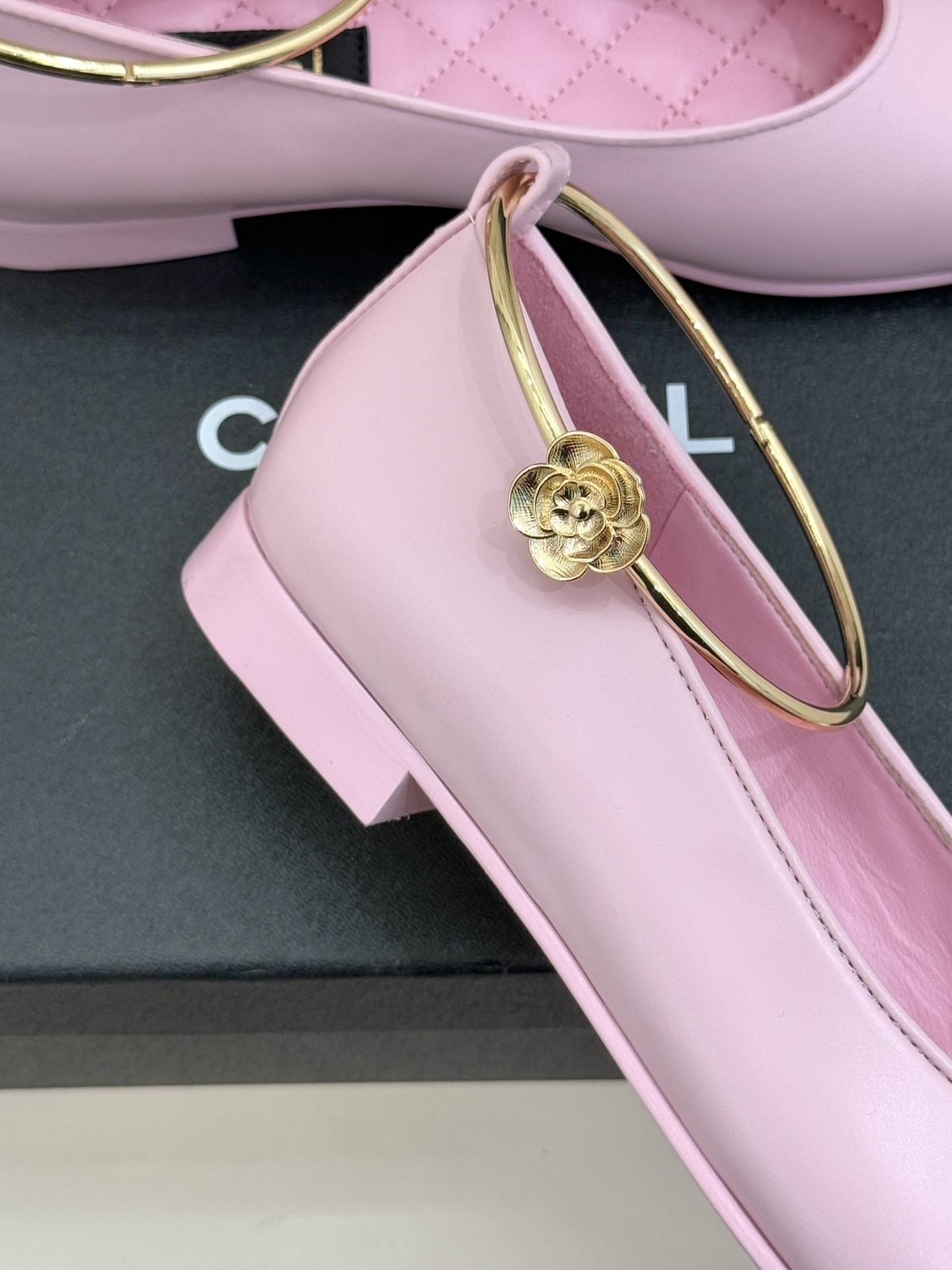 Pair of pink and black Chanel-style ballet flats with gold ankle rings resting on a black box. - Hình 5
