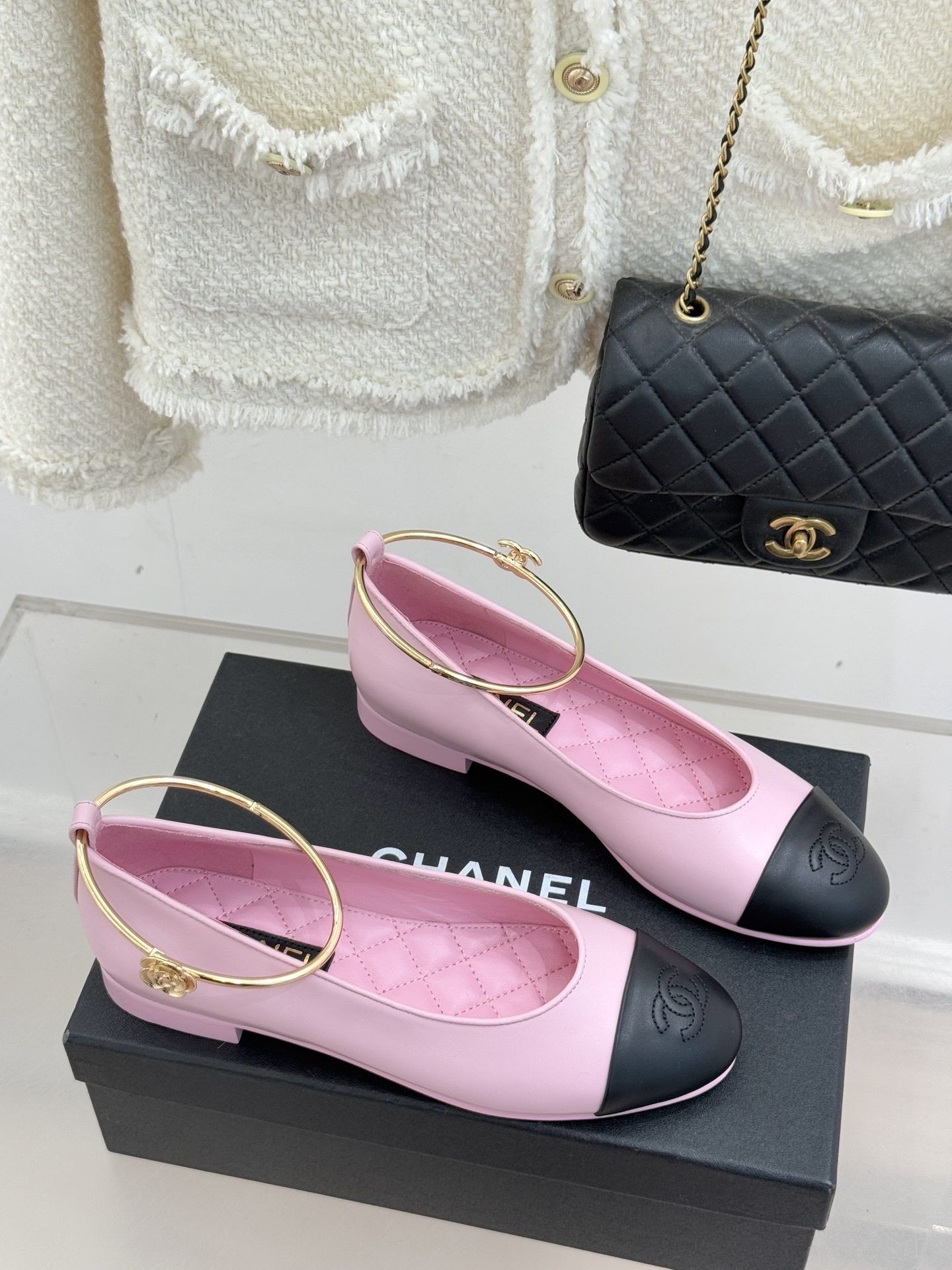 Pair of pink and black Chanel-style ballet flats with gold ankle rings resting on a black box. - Hình 3