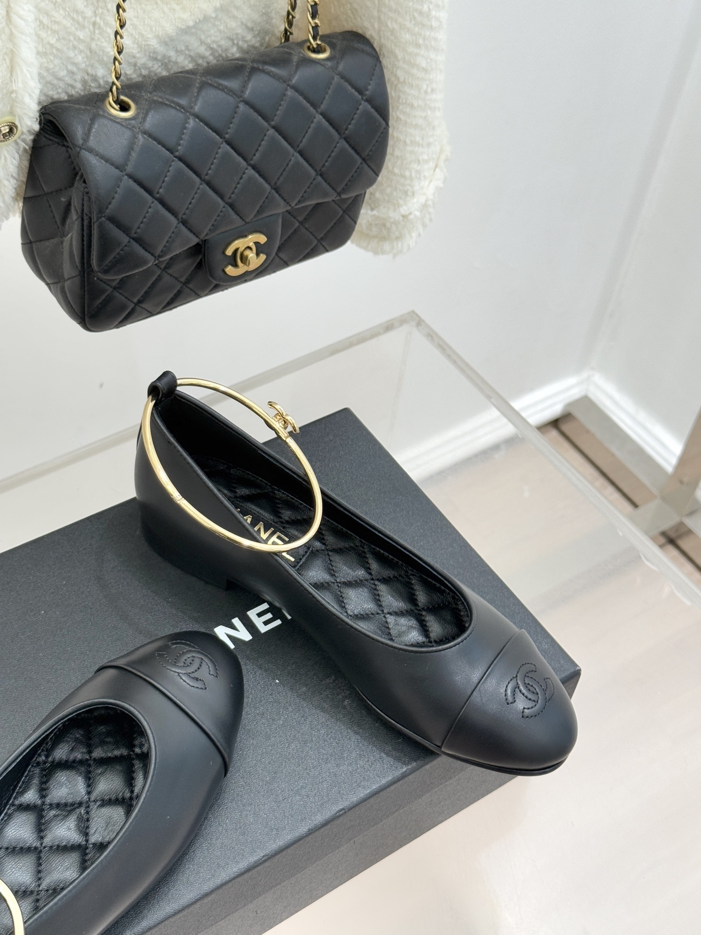 A pair of luxury black leather ballet flats with gold ankle rings and embossed logos on a black designer box. - Hình 5