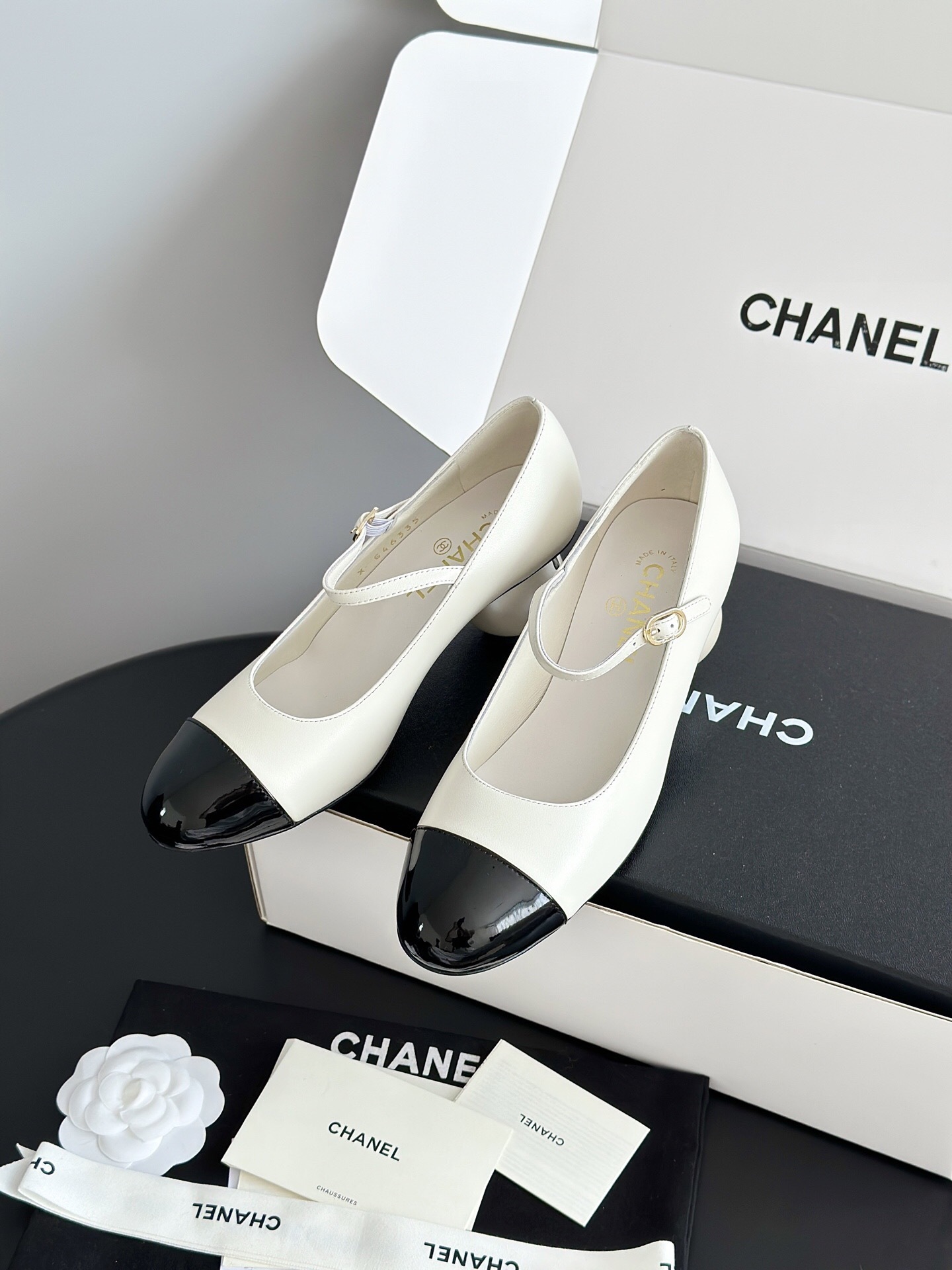 Luxury Chanel Mary Jane pumps in white leather with black patent leather cap toe and block heel, presented in a signature white box. - Hình 2