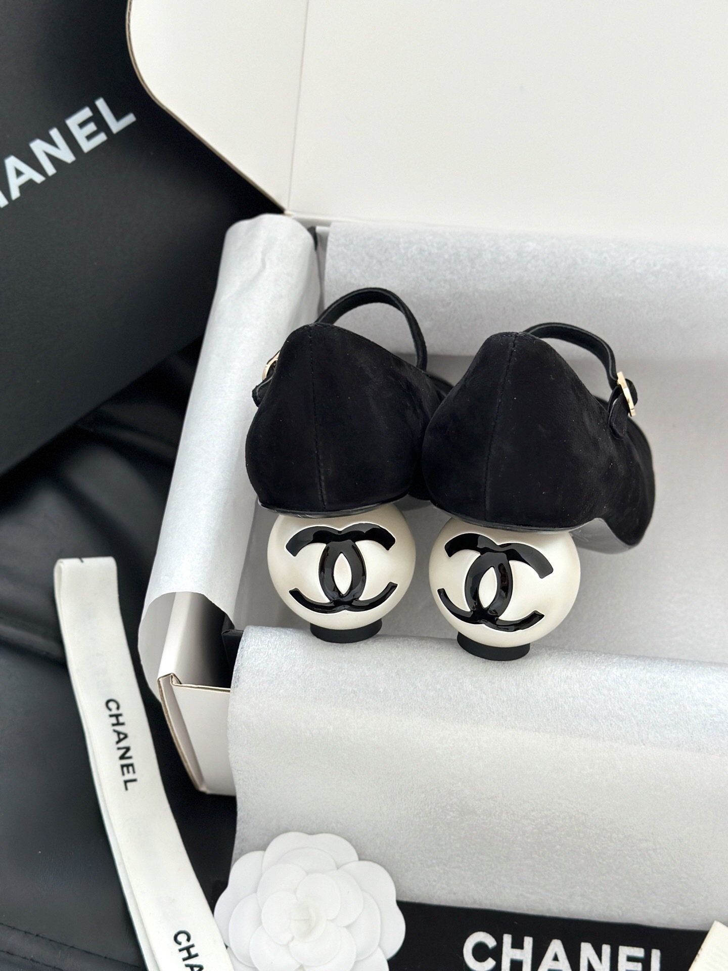 A pair of black Chanel suede Mary Jane pumps with patent leather cap toes and a distinctive white pearl heel displayed in a luxury white box. - Hình 8