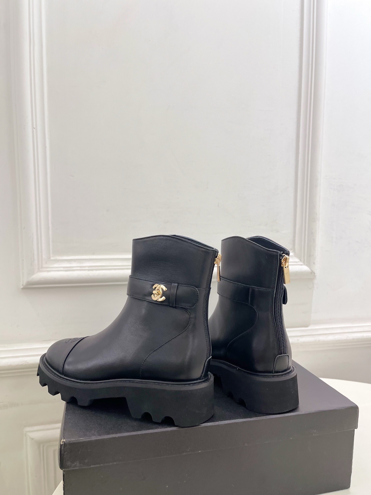 Pair of Chanel black leather ankle boots with gold CC logo and chunky platform sole on a black box. - Hình 7