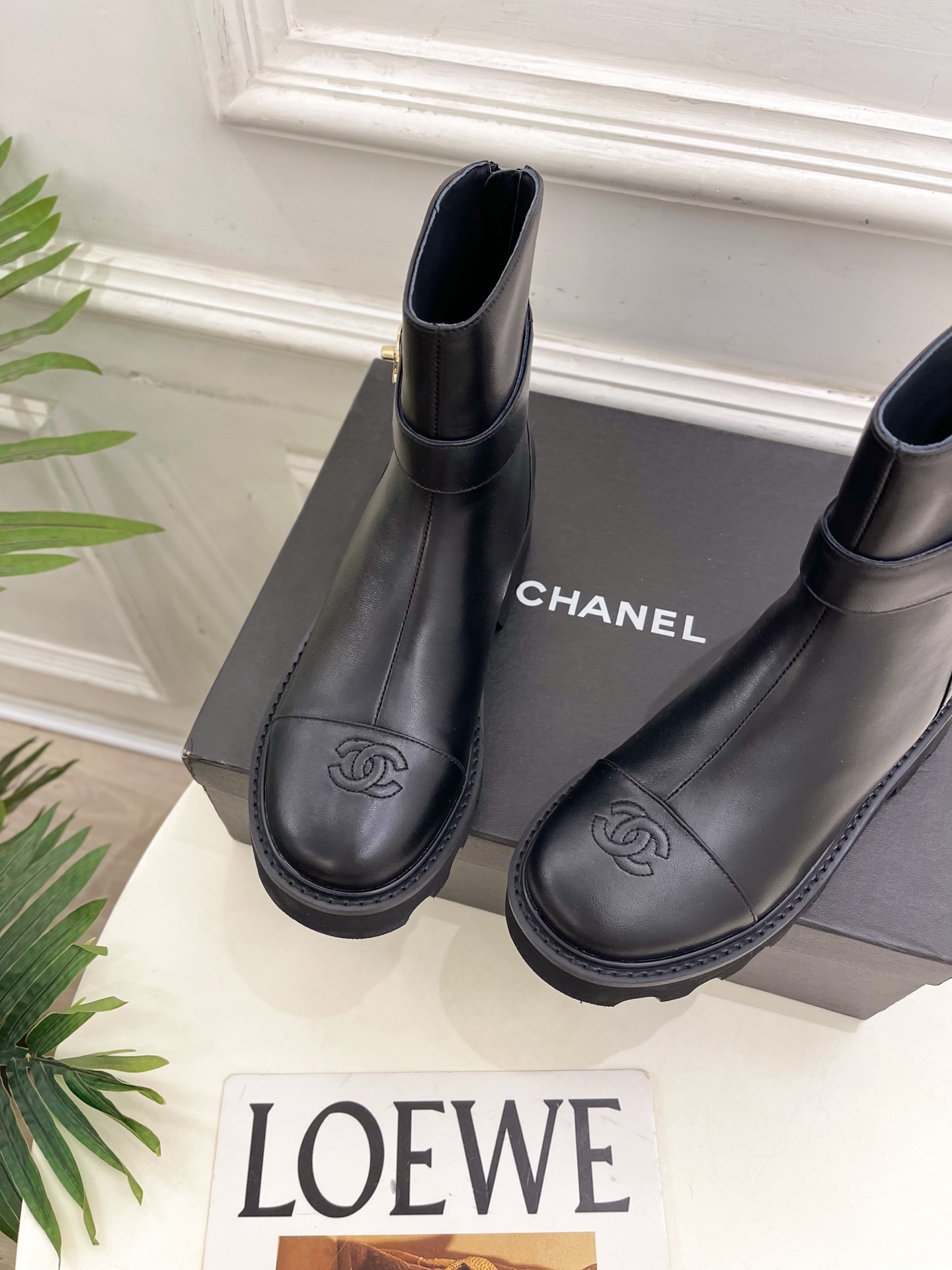 Pair of Chanel black leather ankle boots with gold CC logo and chunky platform sole on a black box. - Hình 6