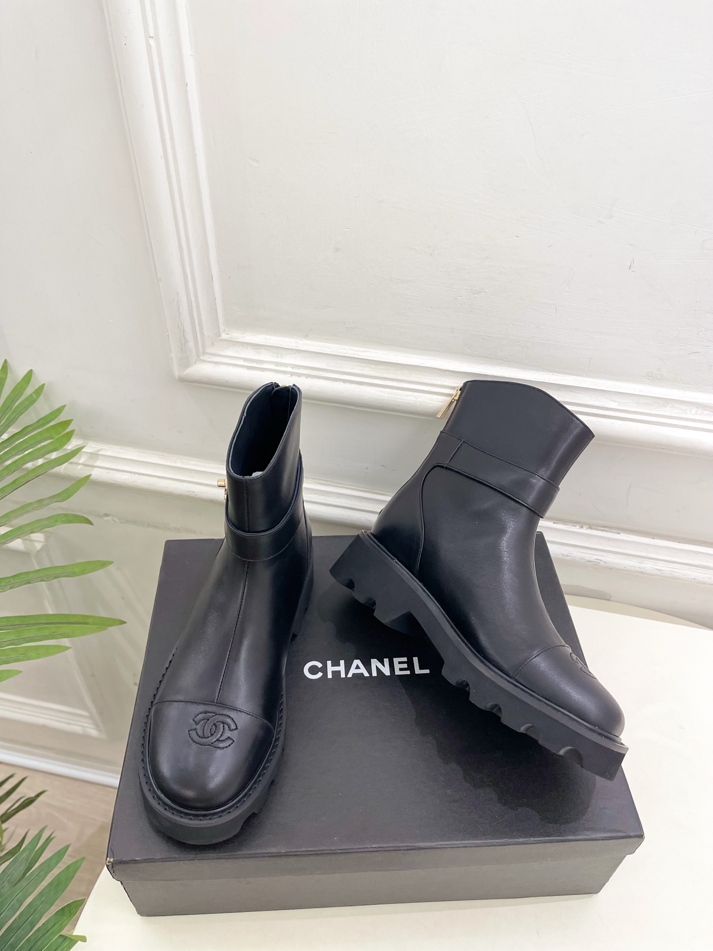Pair of Chanel black leather ankle boots with gold CC logo and chunky platform sole on a black box. - Hình 5