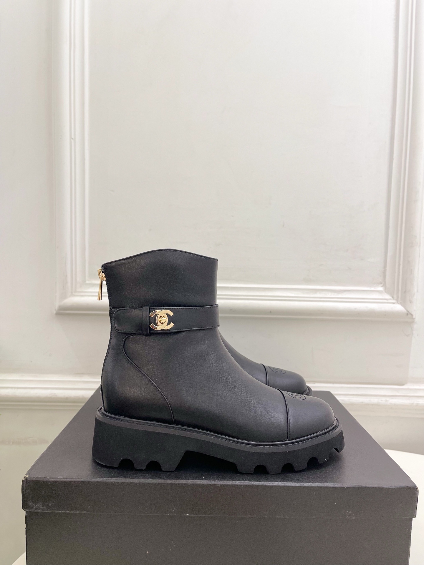 Pair of Chanel black leather ankle boots with gold CC logo and chunky platform sole on a black box. - Hình 2