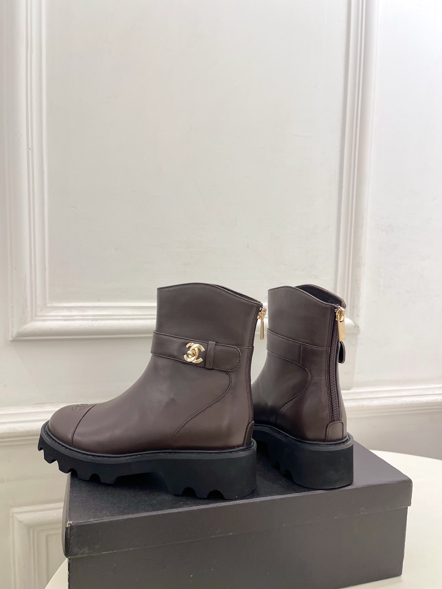 Pair of Chanel dark brown leather ankle boots with CC logo on toe and gold buckle strap on a black box - Hình 8