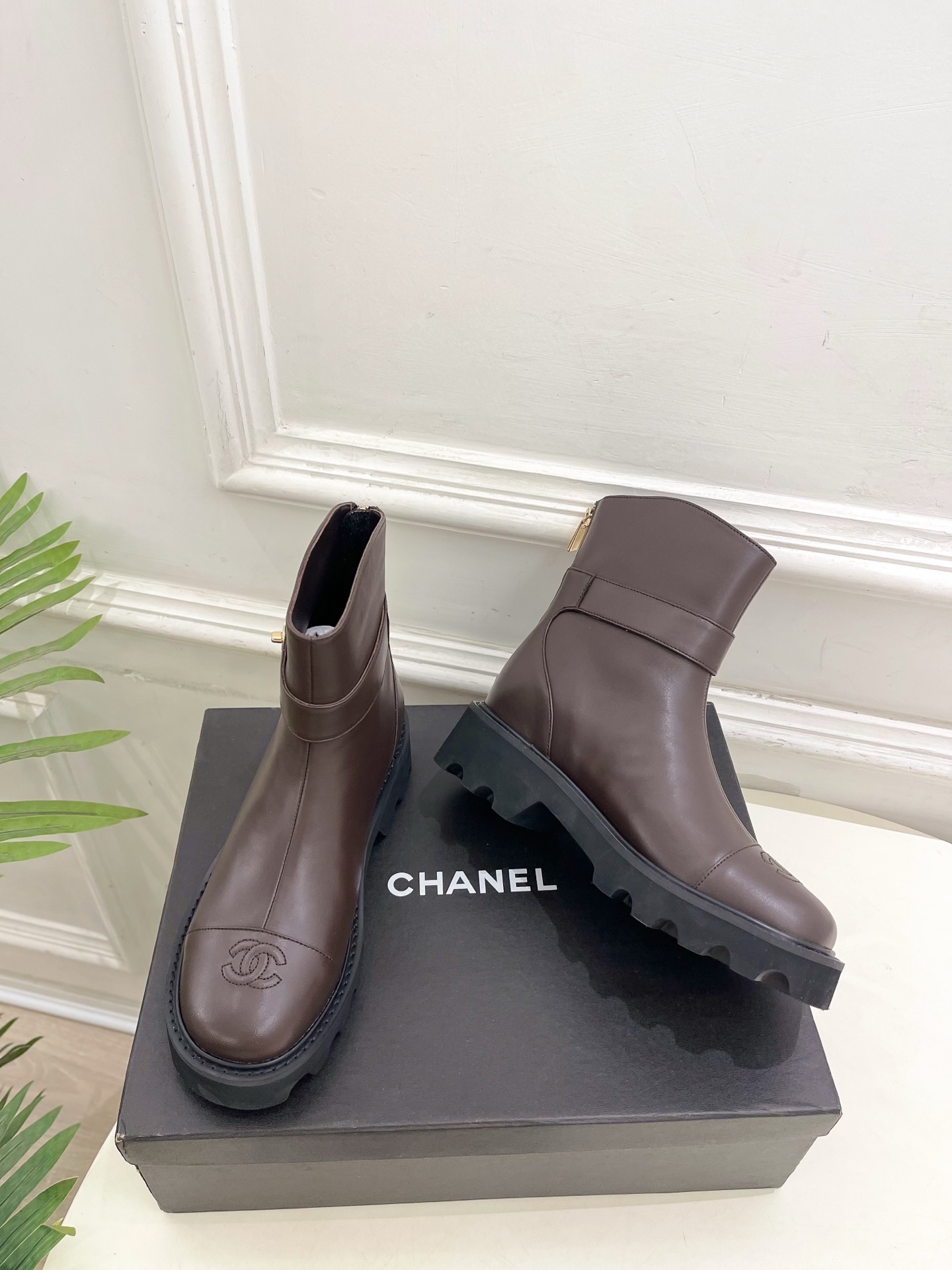 Pair of Chanel dark brown leather ankle boots with CC logo on toe and gold buckle strap on a black box - Hình 5
