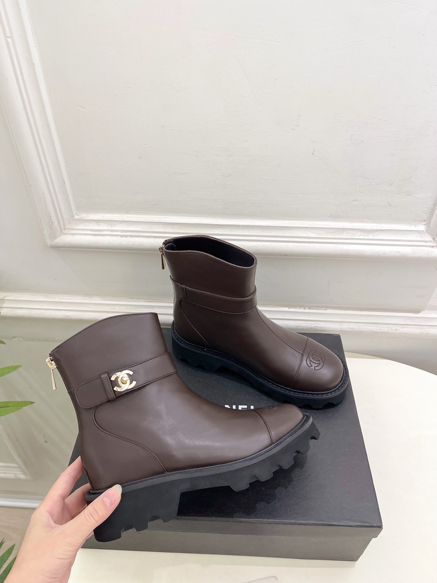 Pair of Chanel dark brown leather ankle boots with CC logo on toe and gold buckle strap on a black box - Hình 4