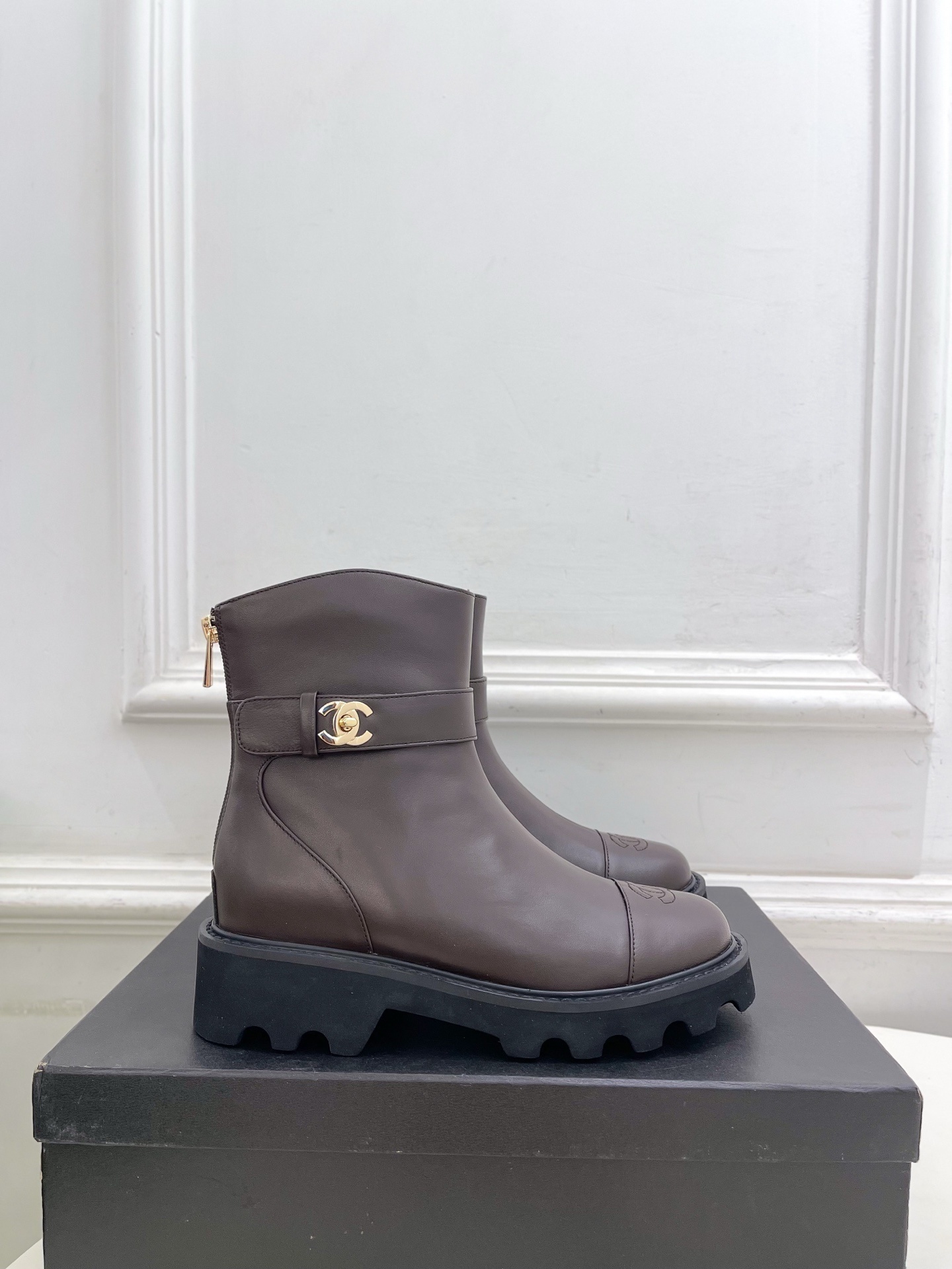 Pair of Chanel dark brown leather ankle boots with CC logo on toe and gold buckle strap on a black box - Hình 2
