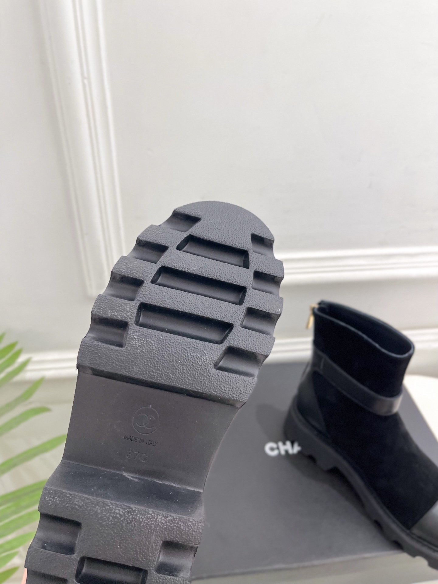 Pair of black Chanel suede ankle boots with leather toe caps and gold CC logo buckles resting on a black box. - Hình 9