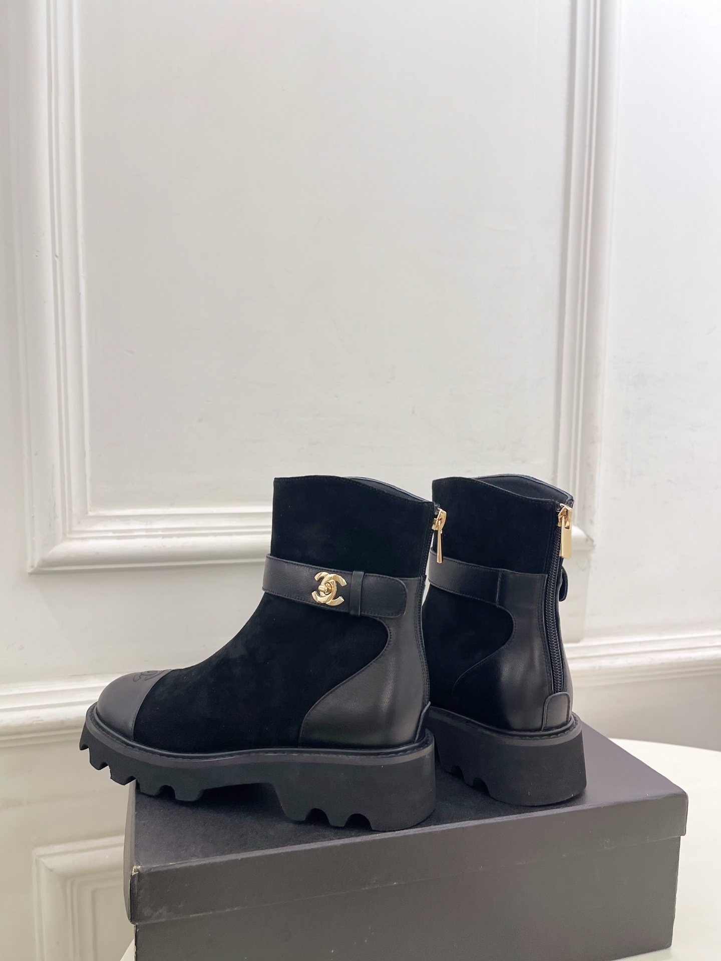 Pair of black Chanel suede ankle boots with leather toe caps and gold CC logo buckles resting on a black box. - Hình 8