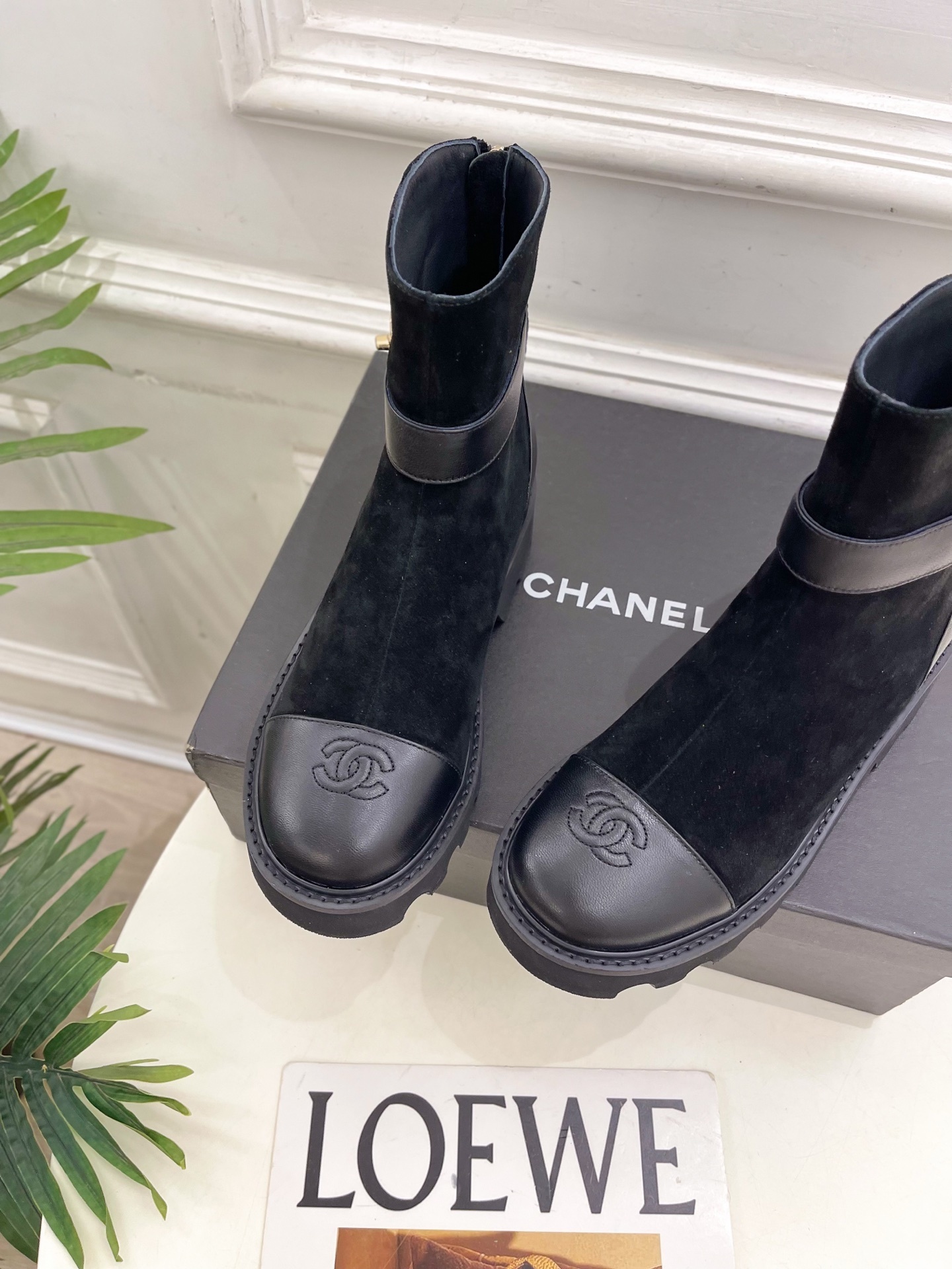 Pair of black Chanel suede ankle boots with leather toe caps and gold CC logo buckles resting on a black box. - Hình 6