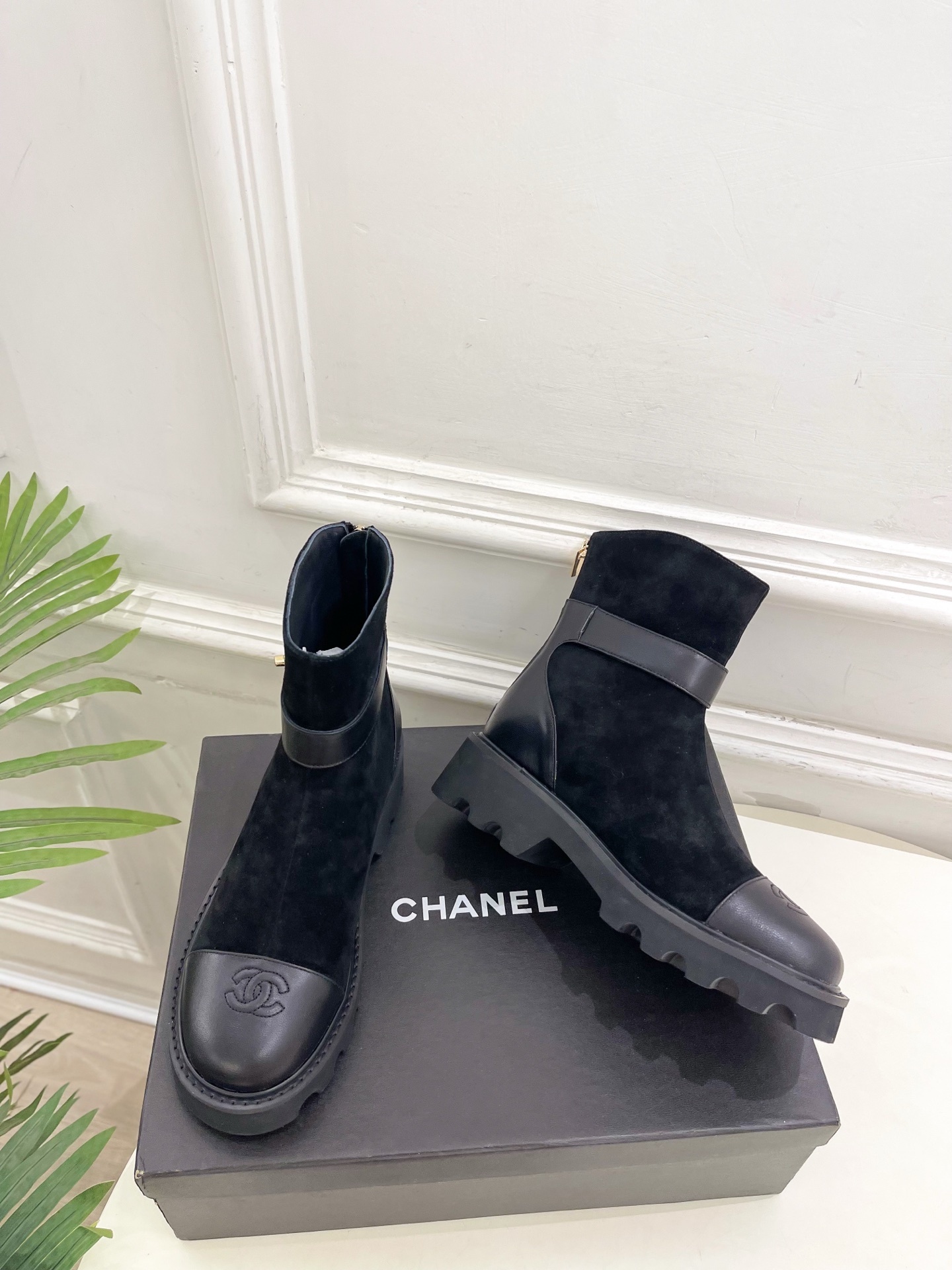 Pair of black Chanel suede ankle boots with leather toe caps and gold CC logo buckles resting on a black box. - Hình 5