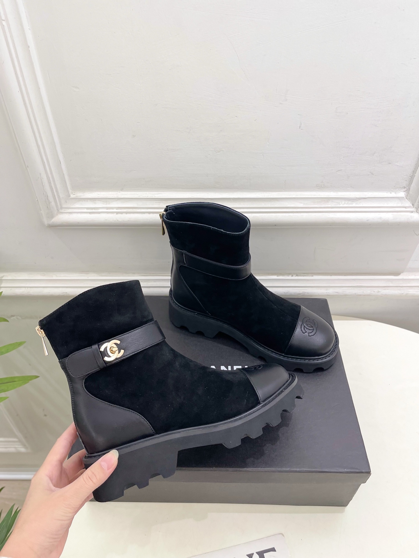 Pair of black Chanel suede ankle boots with leather toe caps and gold CC logo buckles resting on a black box. - Hình 4