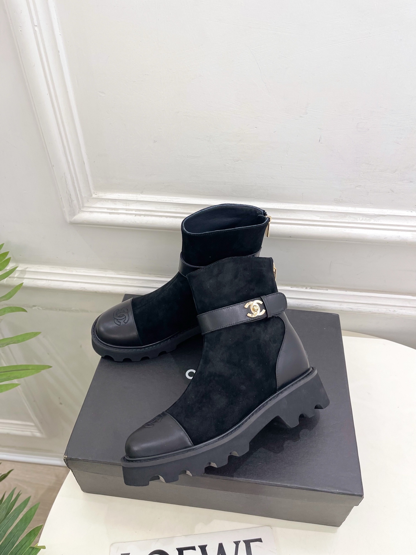 Pair of black Chanel suede ankle boots with leather toe caps and gold CC logo buckles resting on a black box. - Hình 3