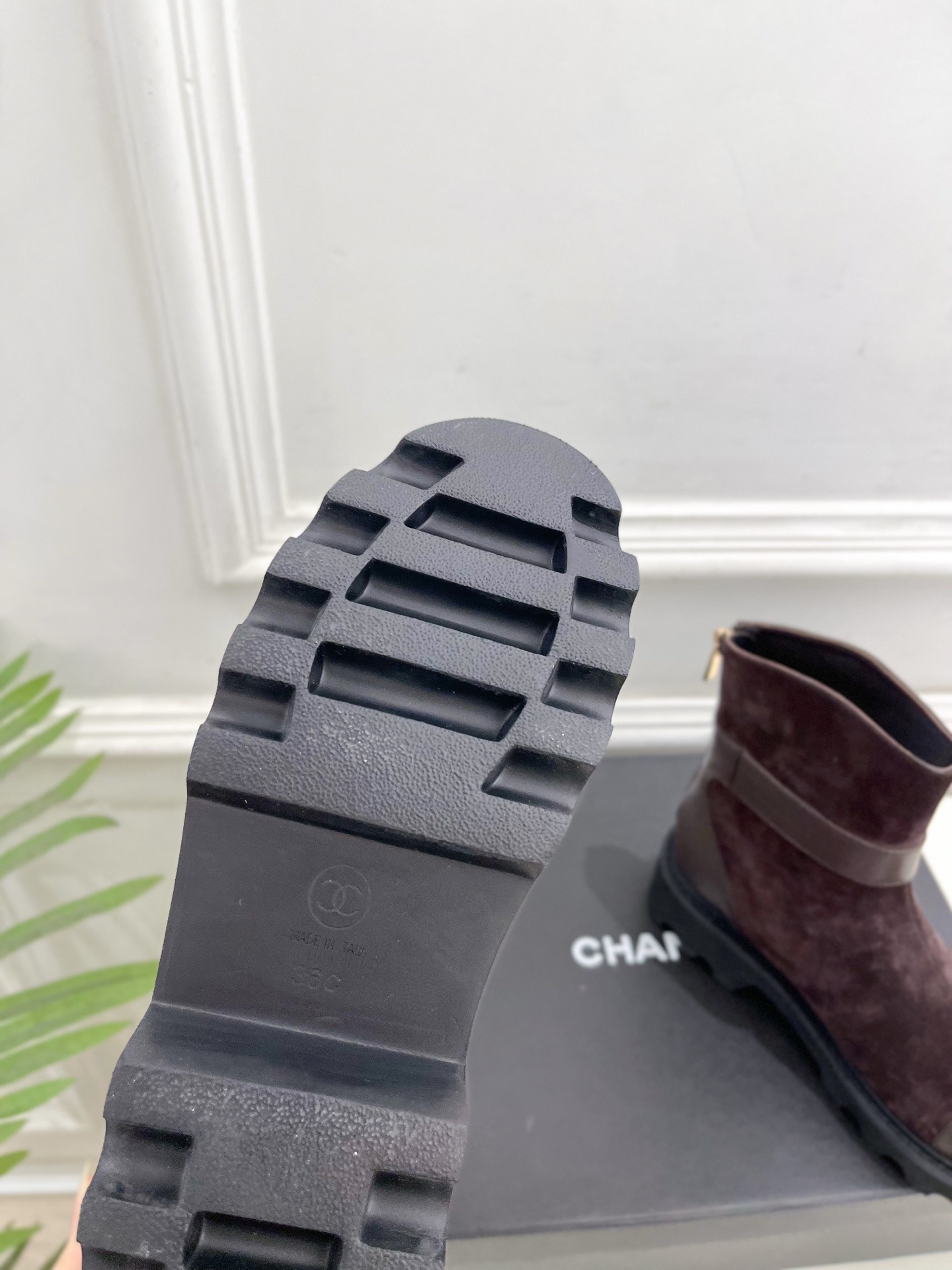 Pair of brown suede Chanel ankle boots with gold CC logo hardware and chunky black lug soles placed on a black shoe box. - Hình 9