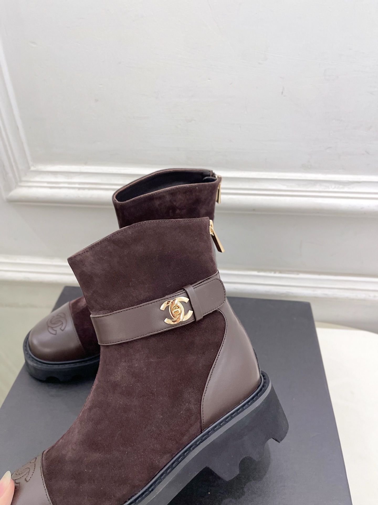 Pair of brown suede Chanel ankle boots with gold CC logo hardware and chunky black lug soles placed on a black shoe box. - Hình 7