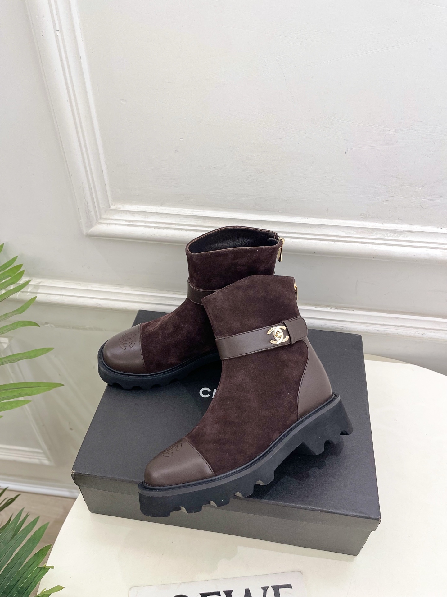 Pair of brown suede Chanel ankle boots with gold CC logo hardware and chunky black lug soles placed on a black shoe box. - Hình 3