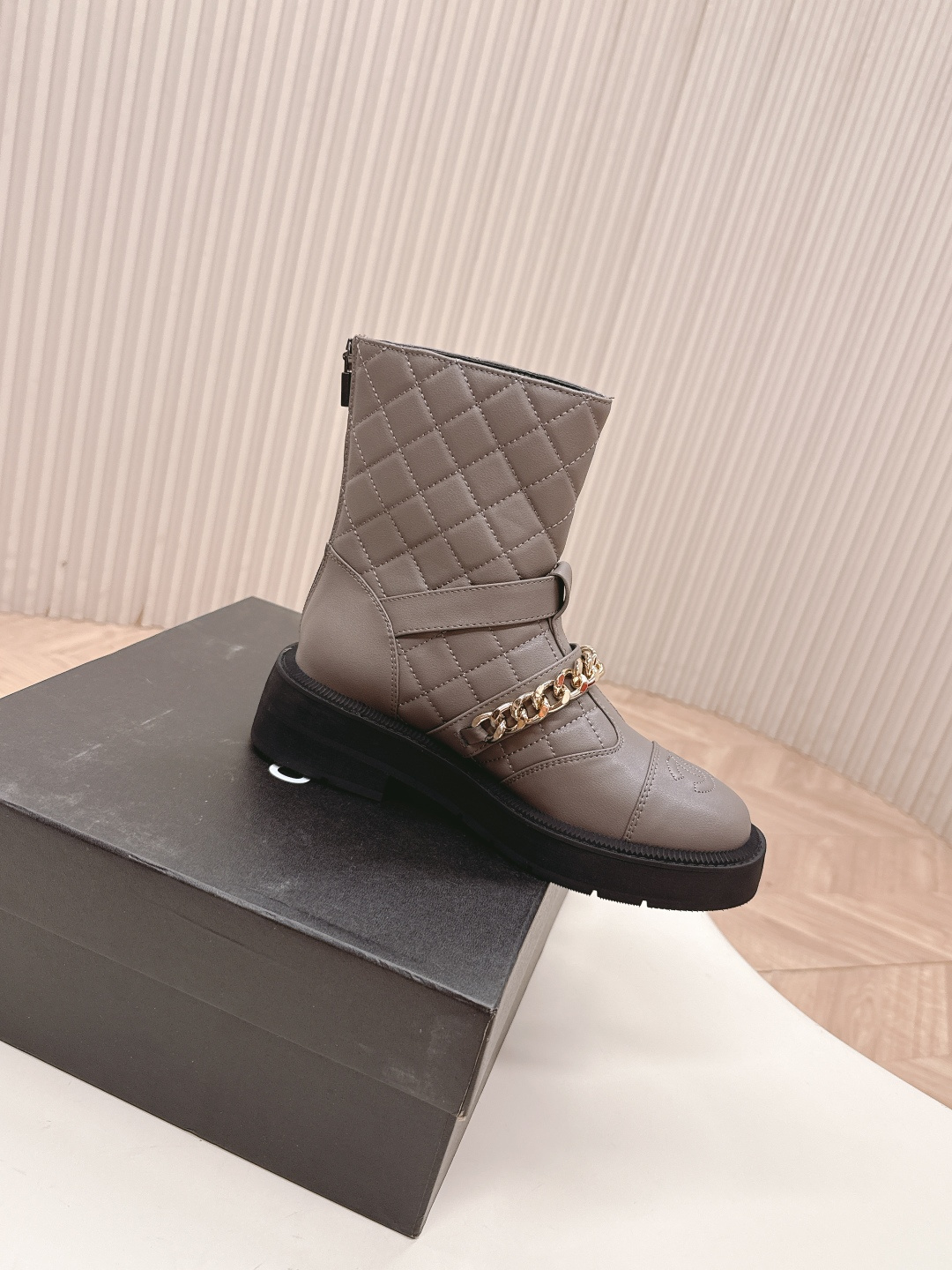 A pair of grey Chanel quilted leather boots with gold chain details and CC logo displayed on a white surface next to a Chanel shoe box. - Hình 9