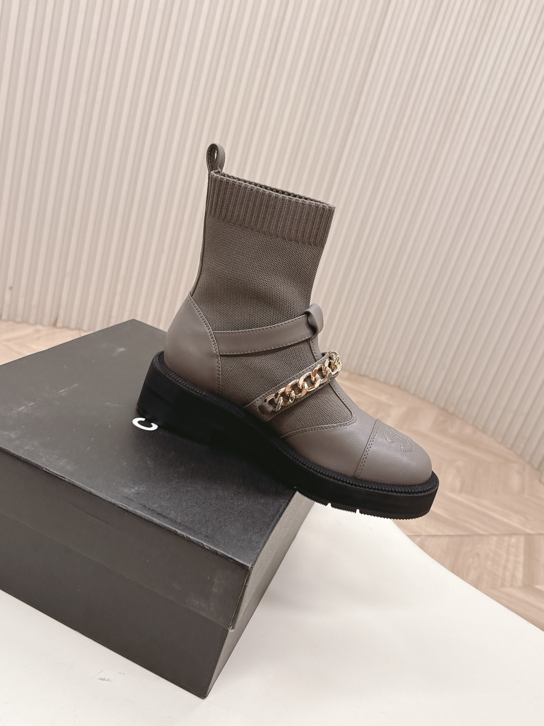 A pair of grey Chanel quilted leather boots with gold chain details and CC logo displayed on a white surface next to a Chanel shoe box. - Hình 7